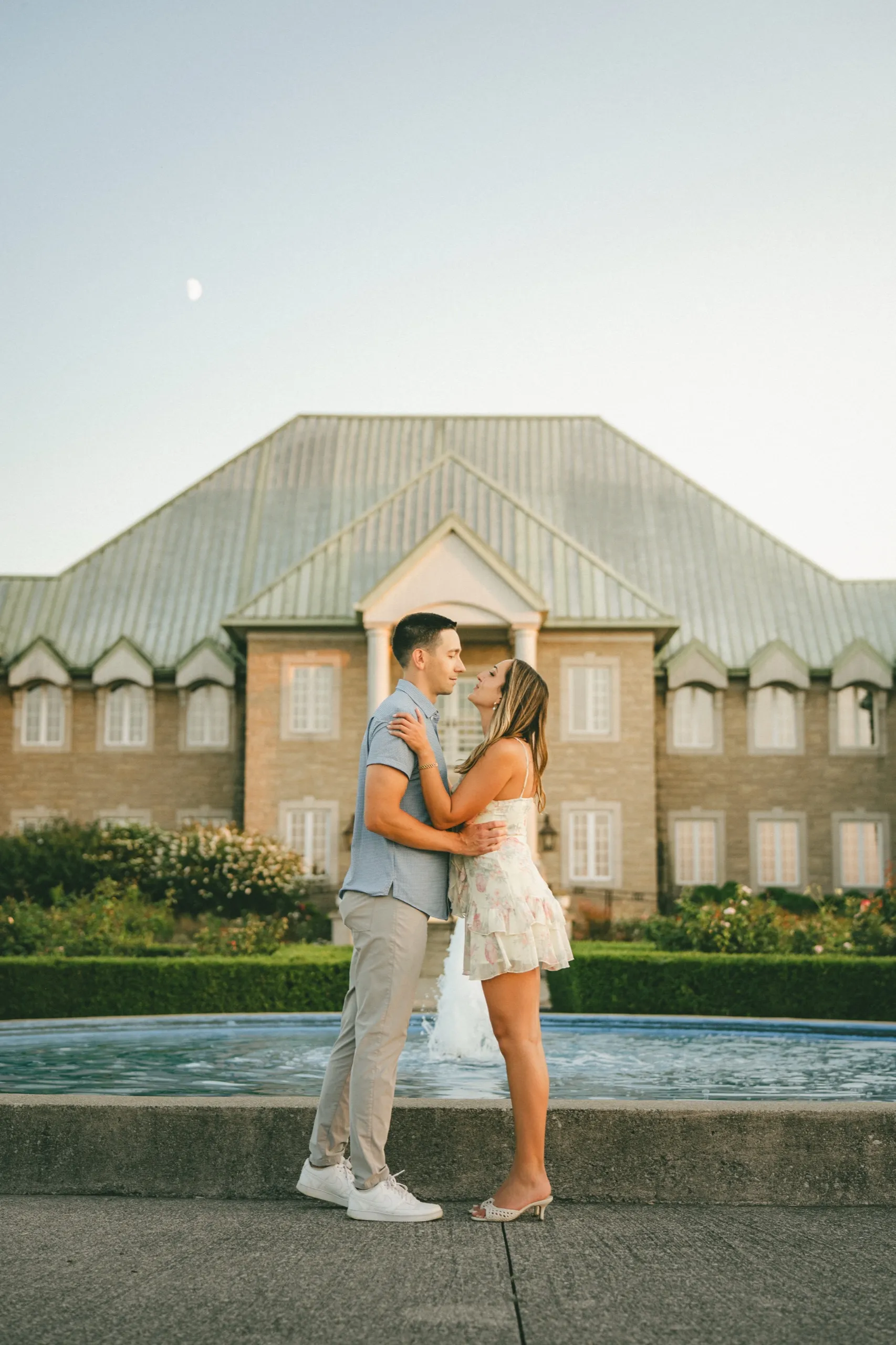The couple by the fountain at dusk with the moon already up over the château roof, by AD Photography