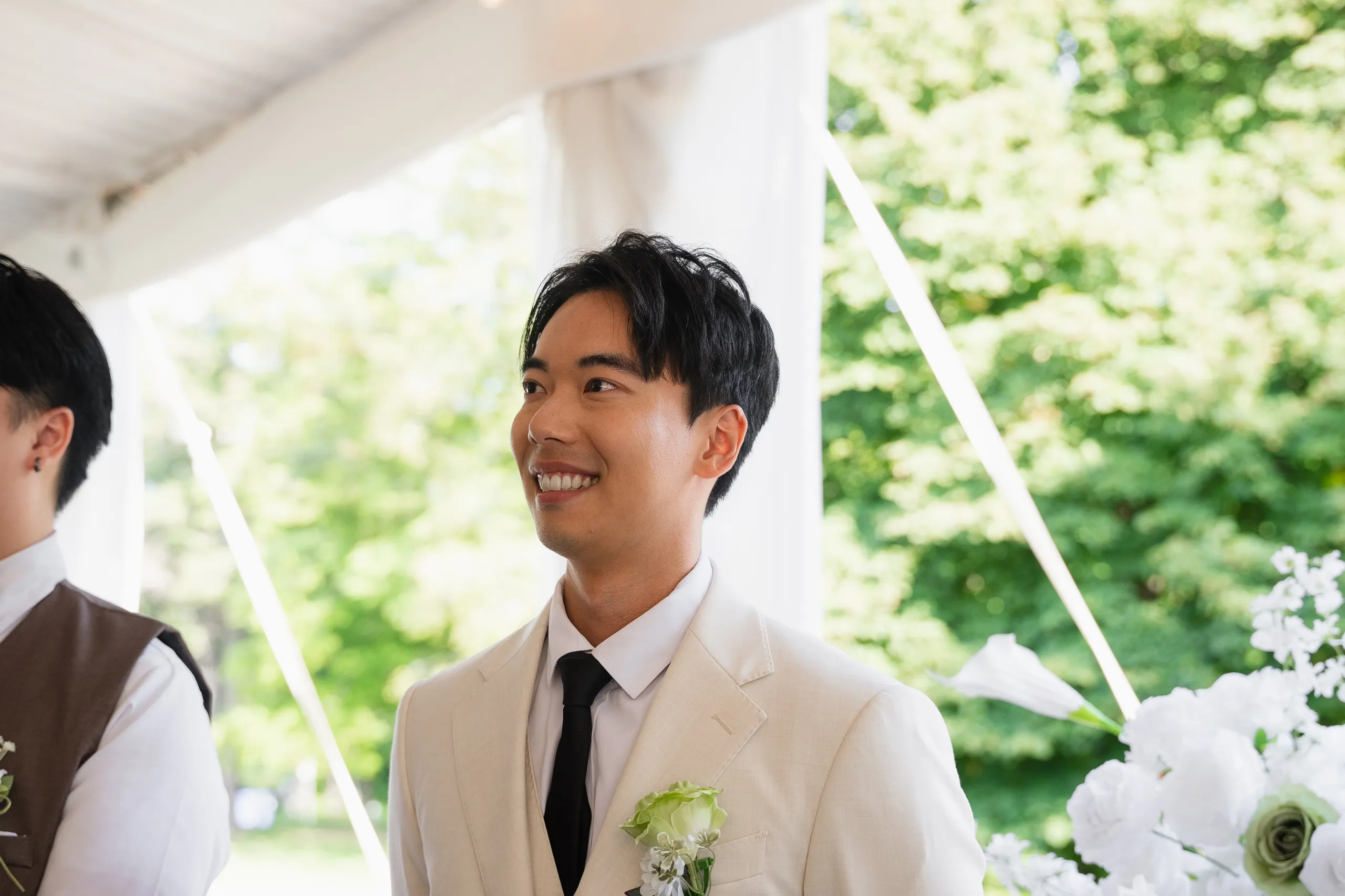 Nelson smiling at the altar beside white ceremony florals at Guild Park and Gardens, by AD Photography