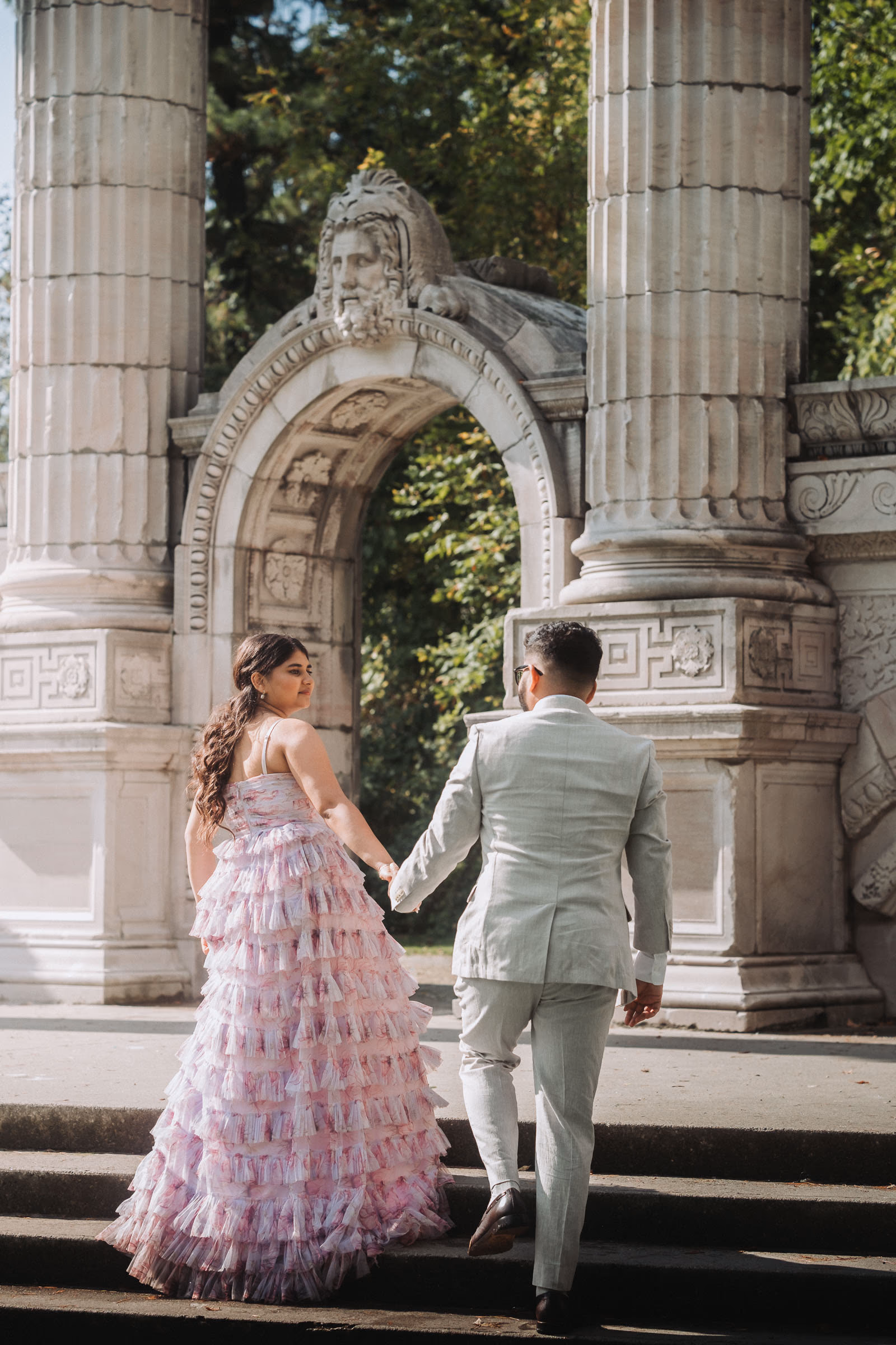 Ayushi and Parth walking up stone steps through a classical archway, Toronto wedding session
