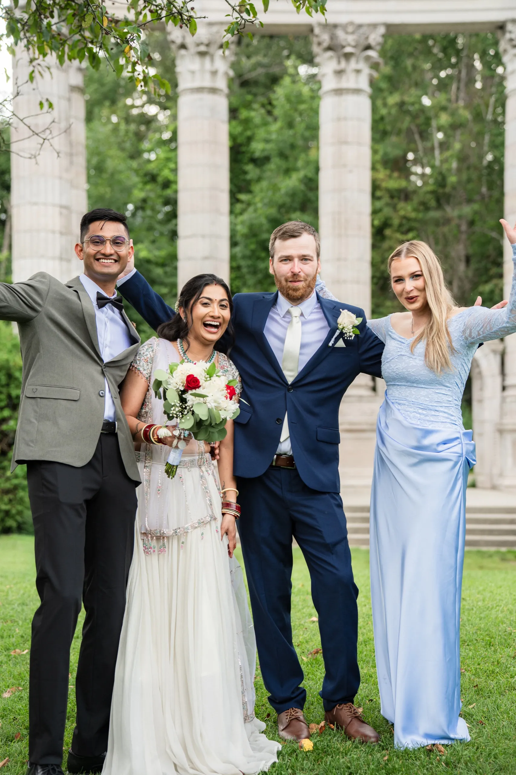 Nidhi and Derek pose with friends throwing their arms wide beneath the columns., by AD Photography