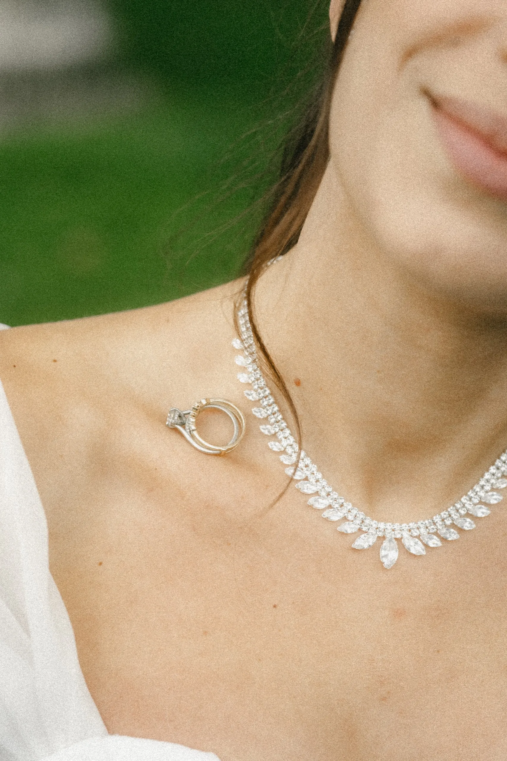 Engagement ring and wedding band balanced on the bride's collarbone beside a diamond necklace, by AD Photography