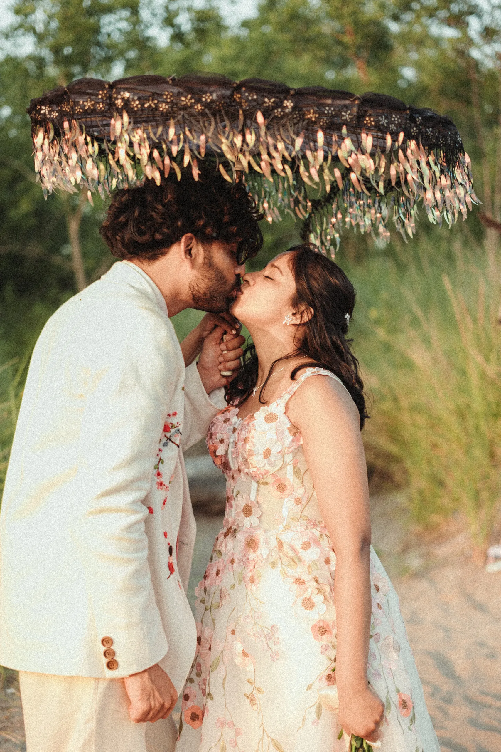 Harsh and Payal kissing beneath a fringed umbrella on the beach at the Toronto Islands, by AD Photography