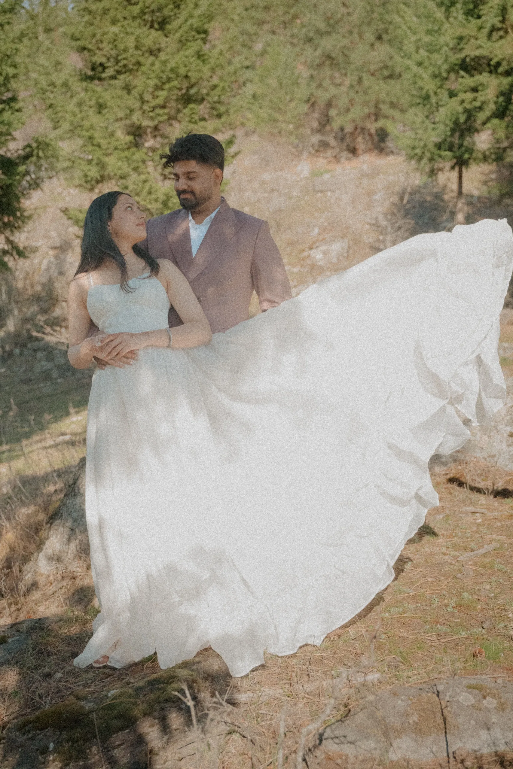 The bride sweeping her gown across a rock while Kamal steadies her from behind, by AD Photography
