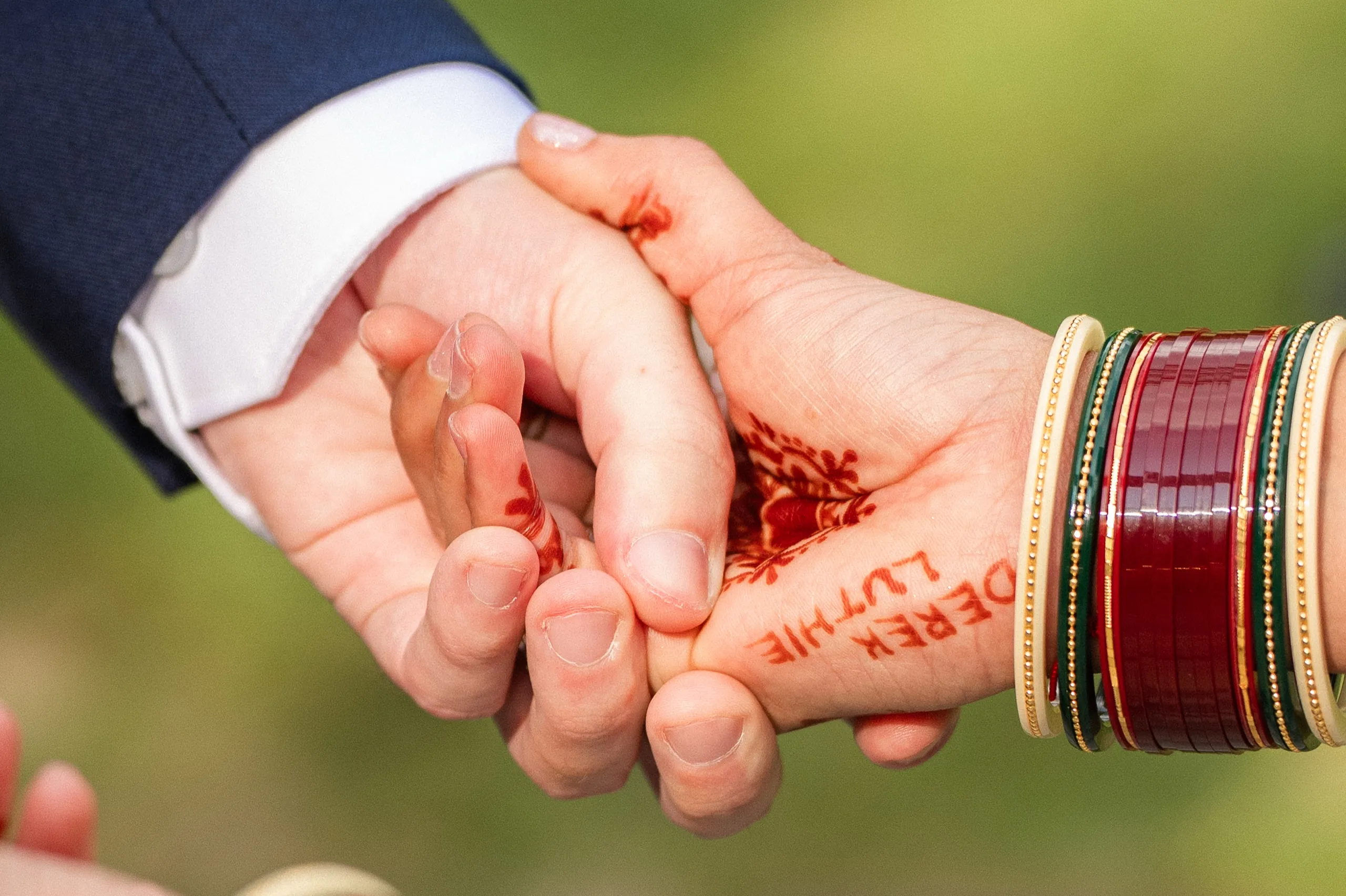 Close on hands entwined, henna spelling out their names across Nidhi's open palm., by AD Photography