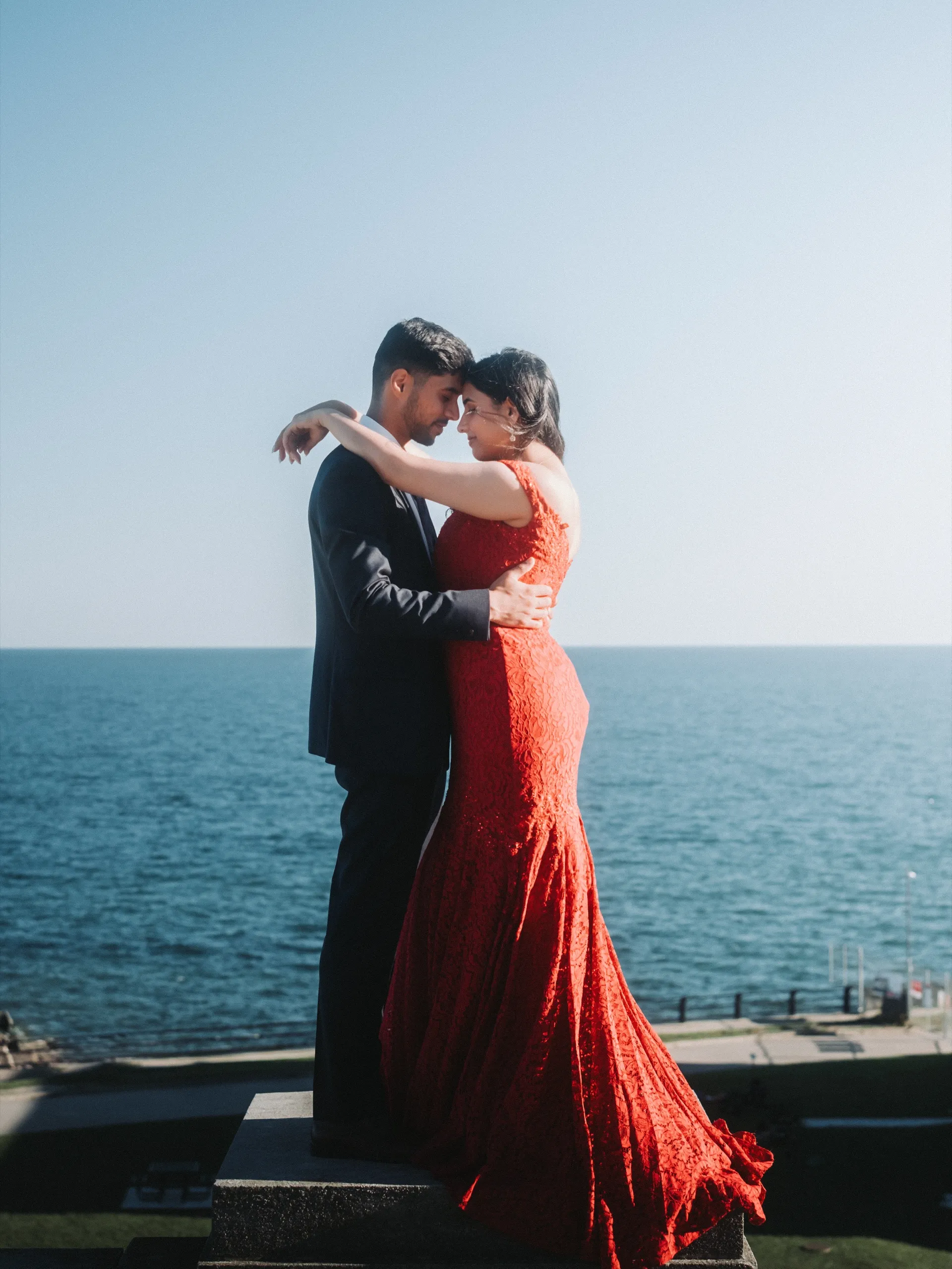 Swati and Saksham touch foreheads on a stone plinth high above Lake Ontario, by AD Photography