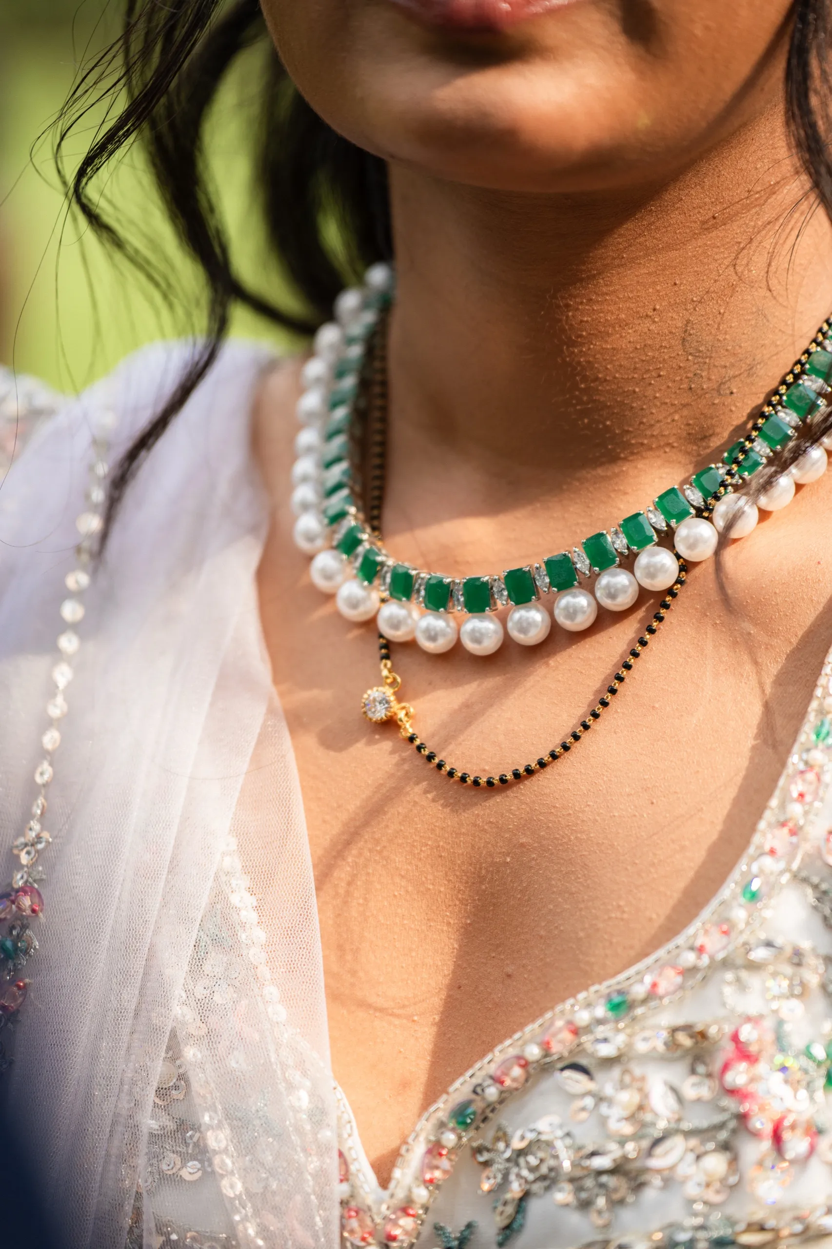 A close look at Nidhi's layered pearl, emerald, and mangalsutra necklaces in the sun., by AD Photography