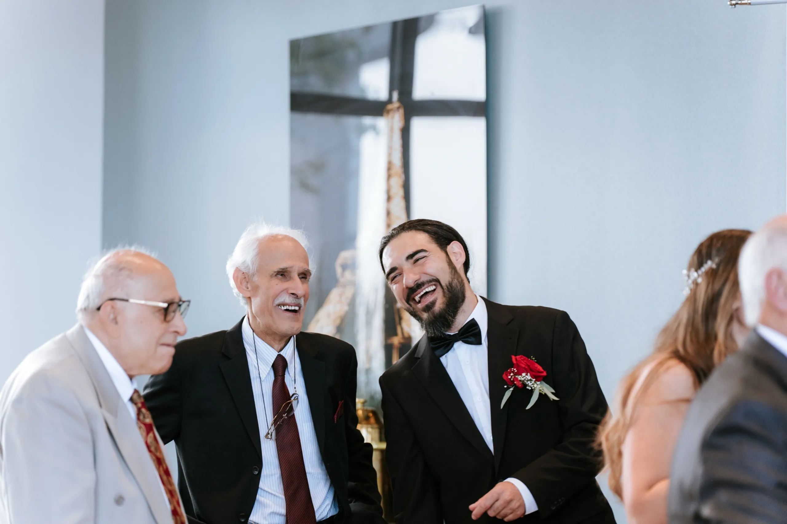 Moe laughing with two family elders in front of the artwork on the pale blue wall, by AD Photography