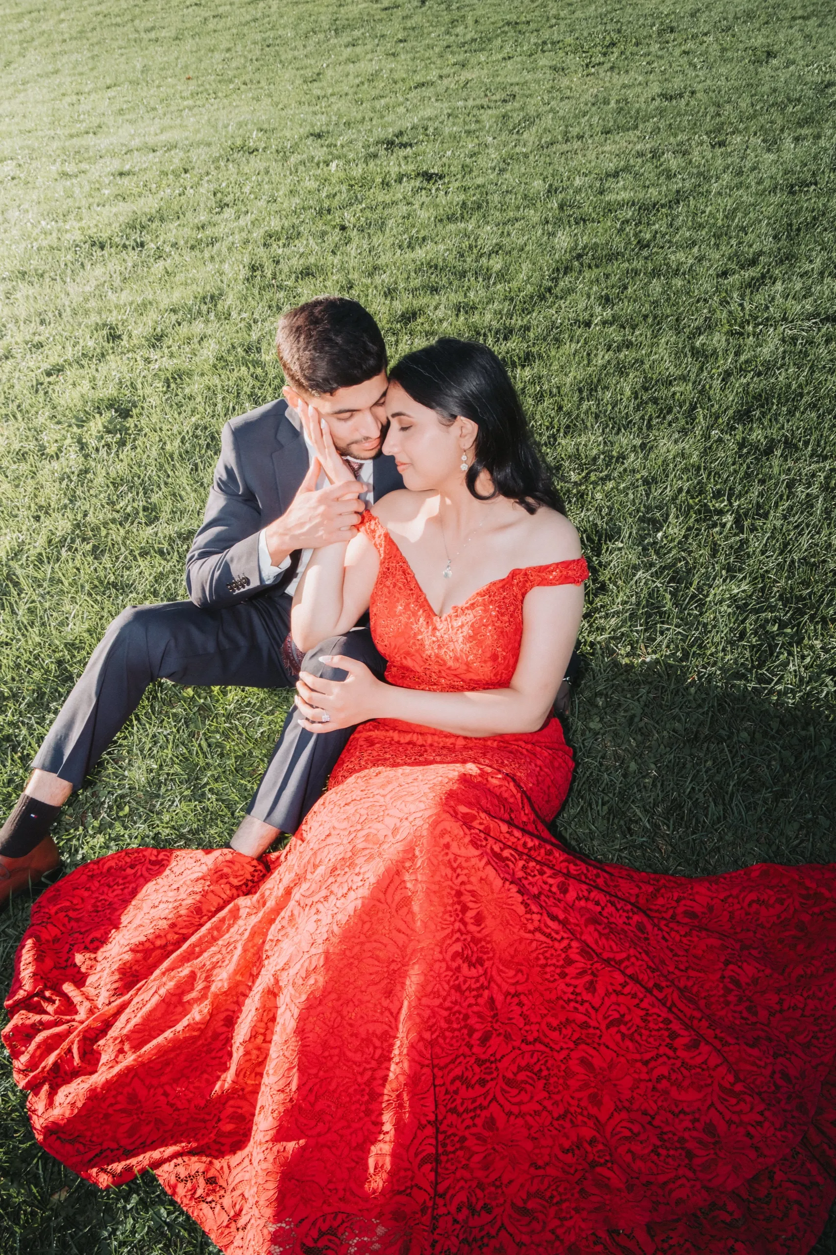 Saksham nuzzles Swati on the sunlit lawn, lace train fanned across the grass, by AD Photography