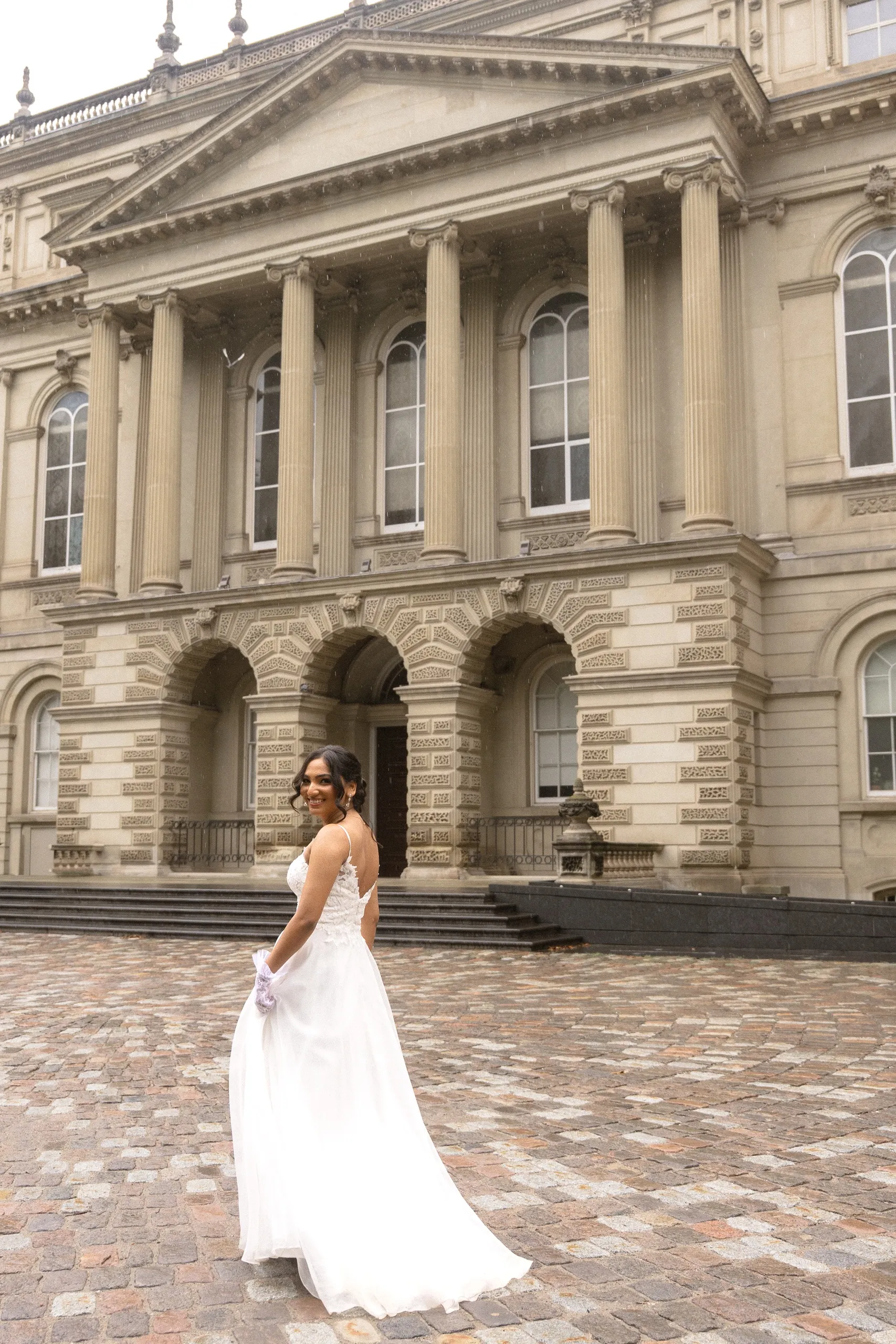 Bride looks back with the Osgoode Hall colonnade behind her, by AD Photography