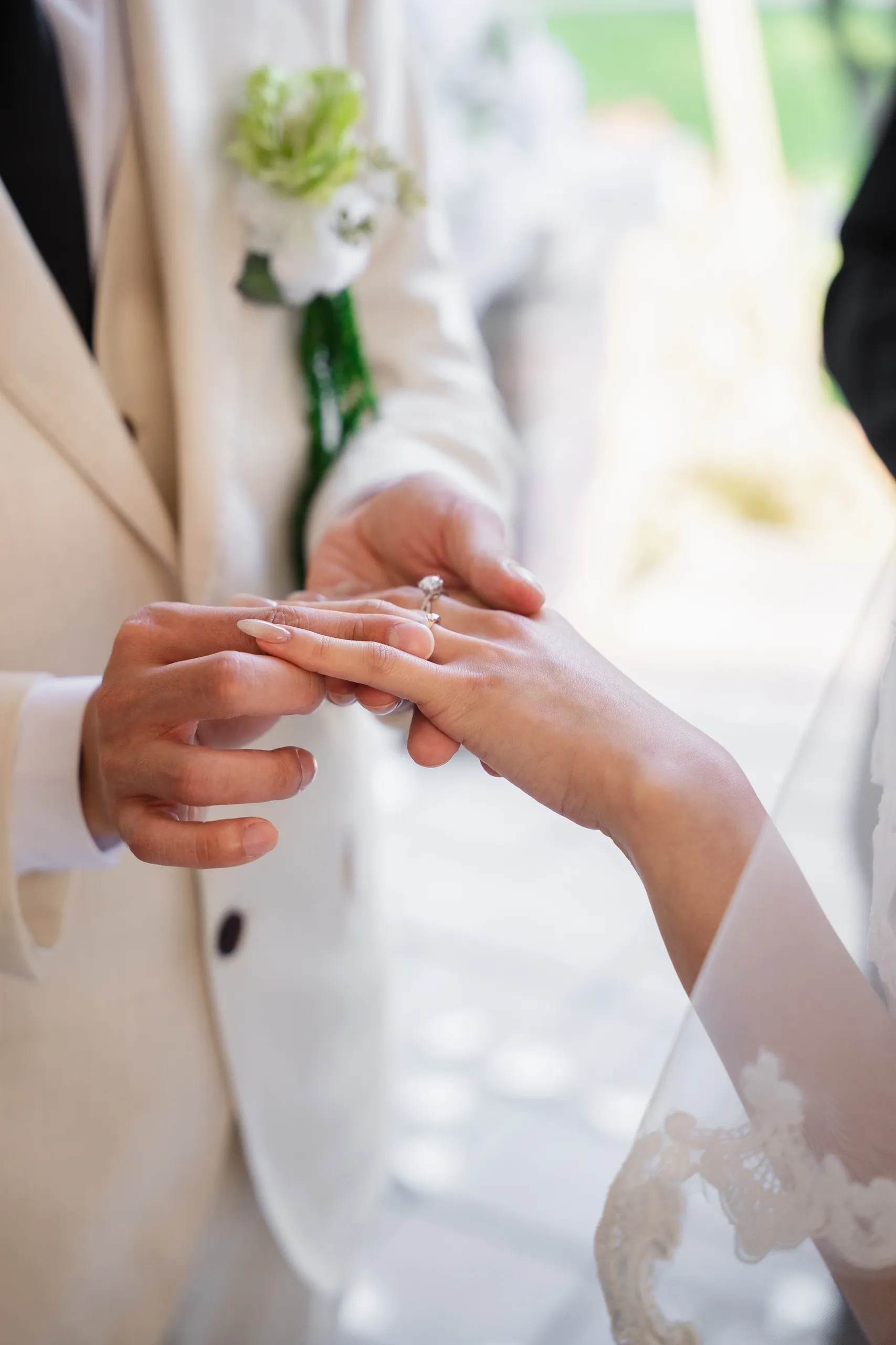 Close crop on the ring sliding onto Josie's finger, boutonniere soft in the background, by AD Photography