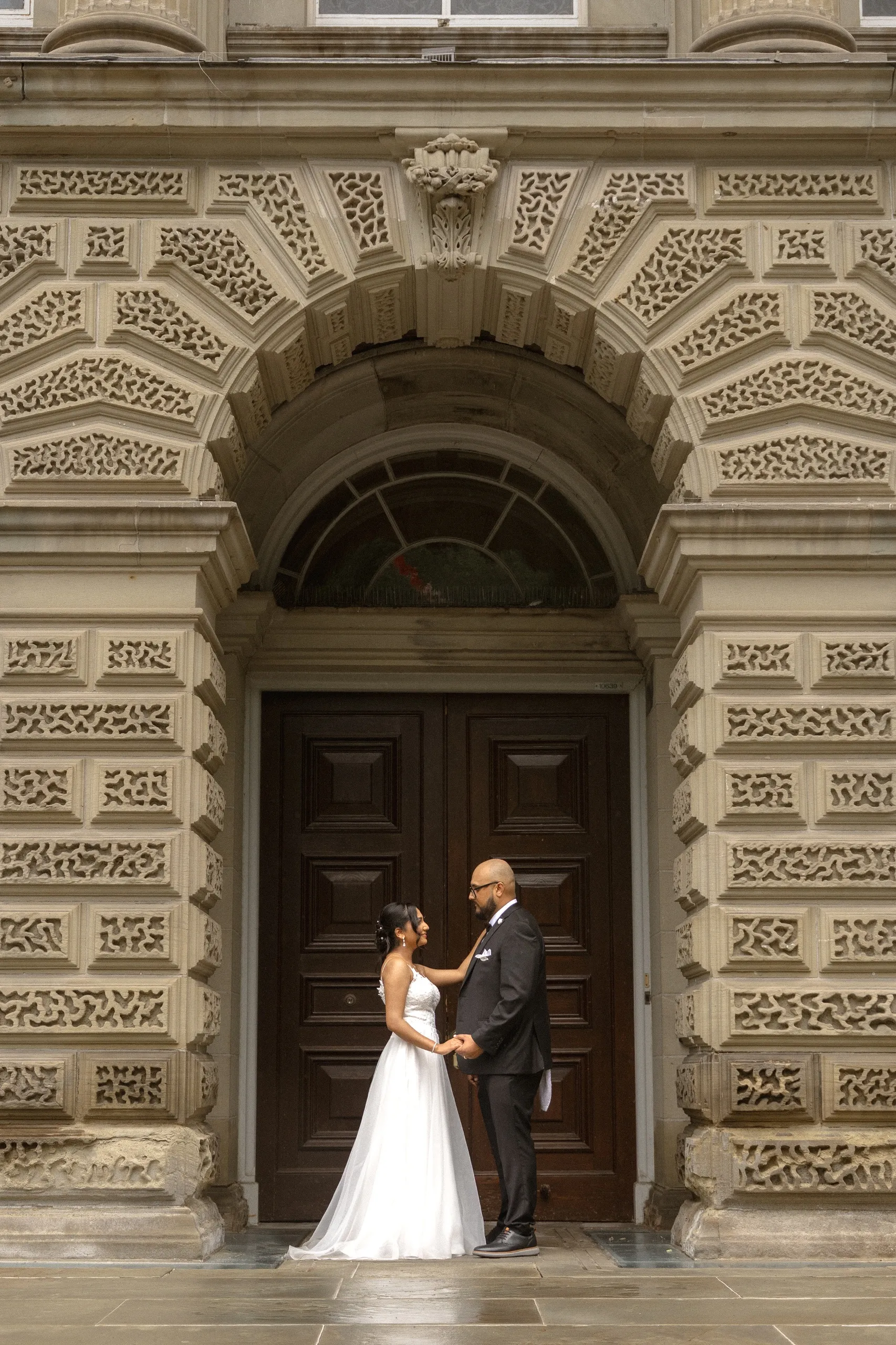 Bride and groom beneath the carved stone arch at Osgoode Hall, by AD Photography