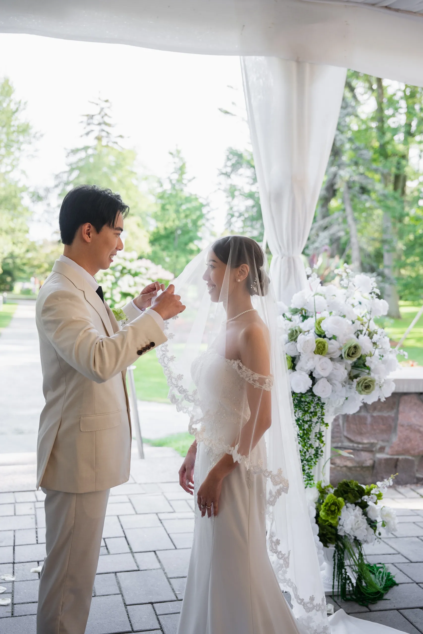 Nelson lifting Josie's veil beside the tall white and green ceremony florals, by AD Photography