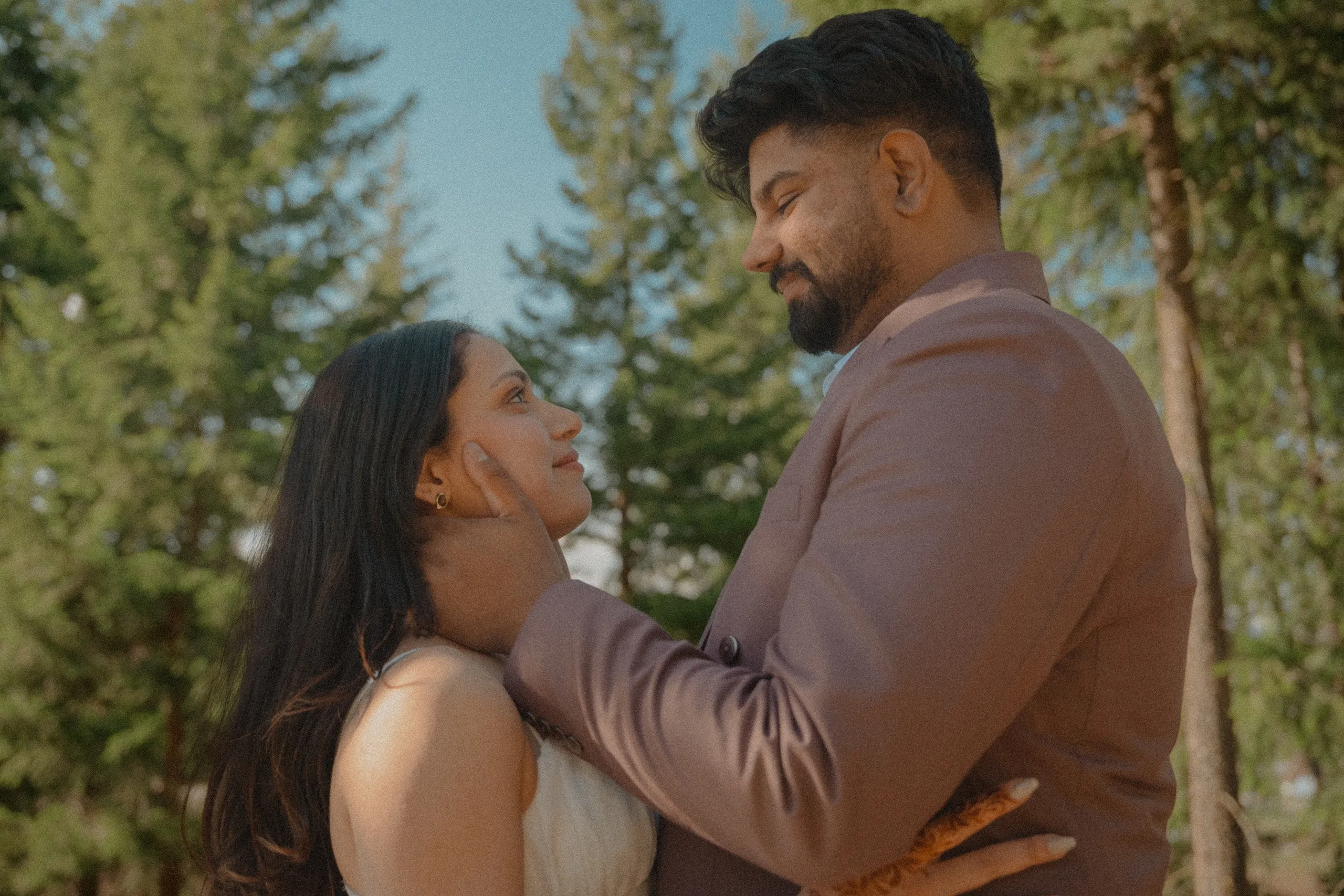 Kamal cupping Mehak's face among tall pines under an open blue sky, by AD Photography