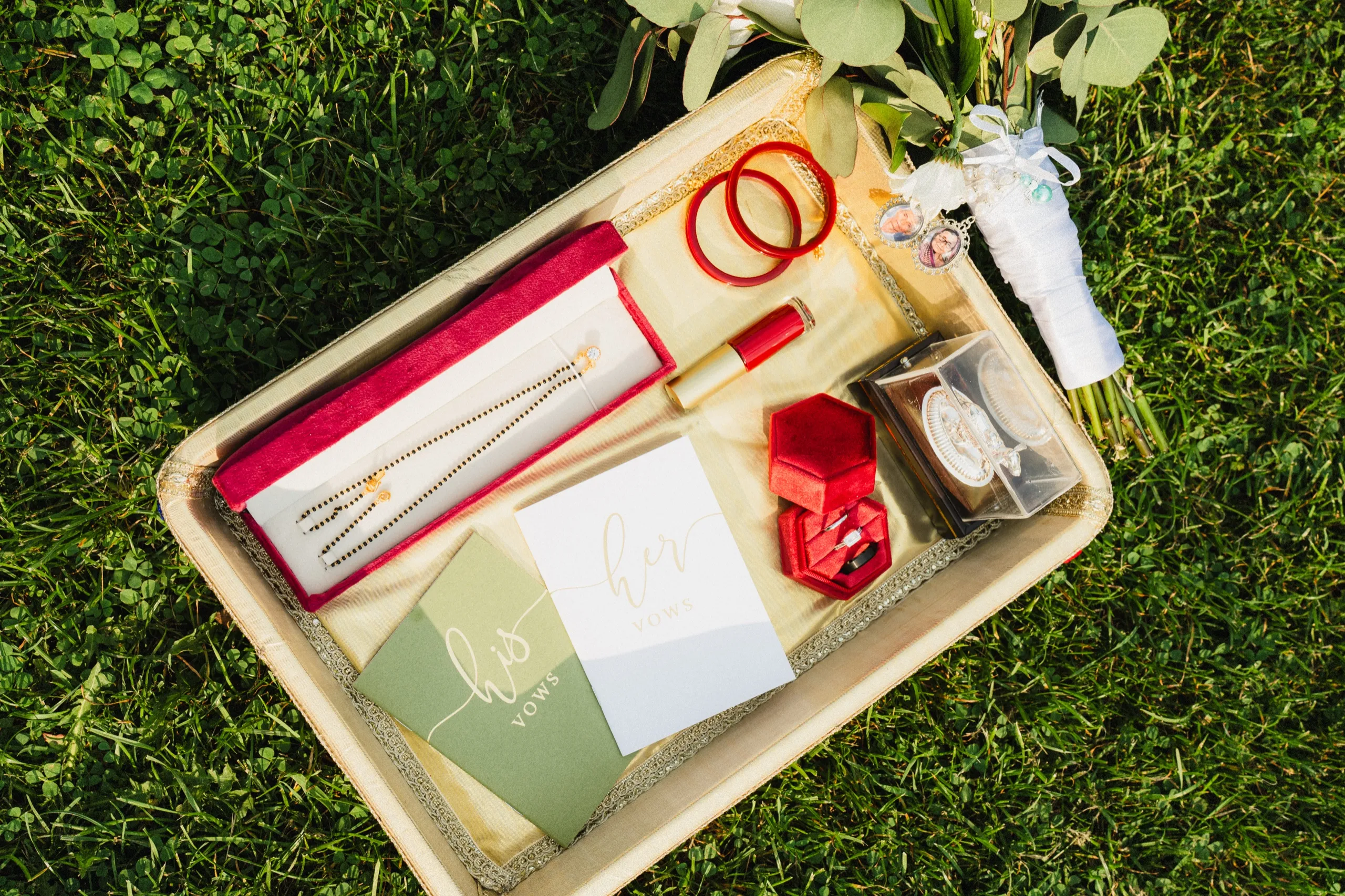 Overhead, the his and her vows cards rest beside rings, bangles, and photo lockets., by AD Photography