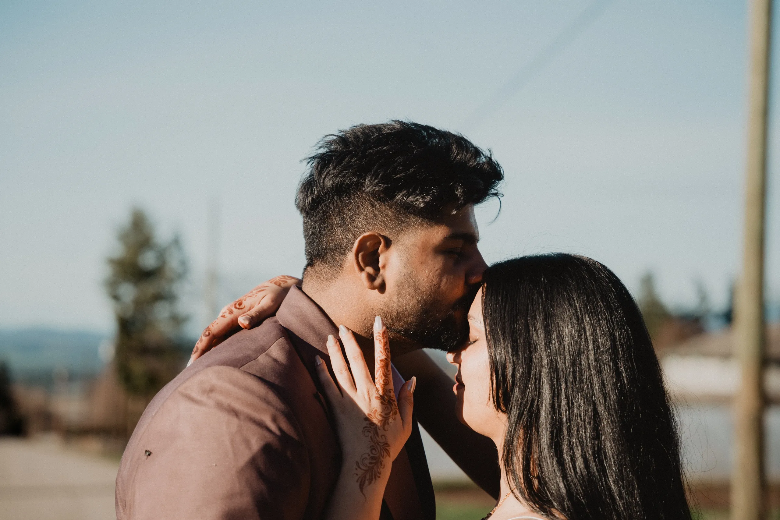 Kamal kissing Mehak's forehead on the farm road, her henna hand on his jaw, by AD Photography