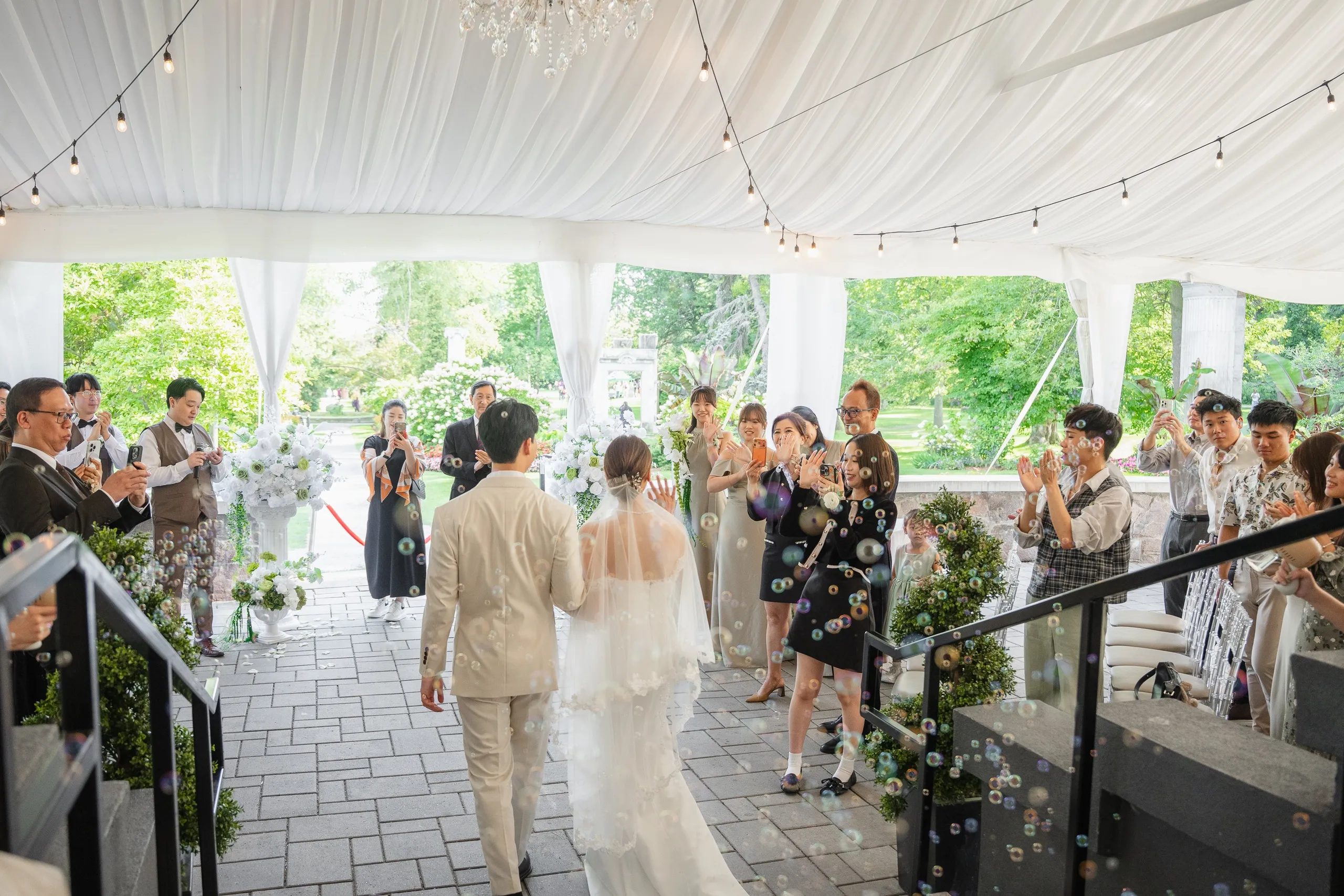 Wide view through bubbles and clapping guests as the couple leave the Guild Park tent, by AD Photography