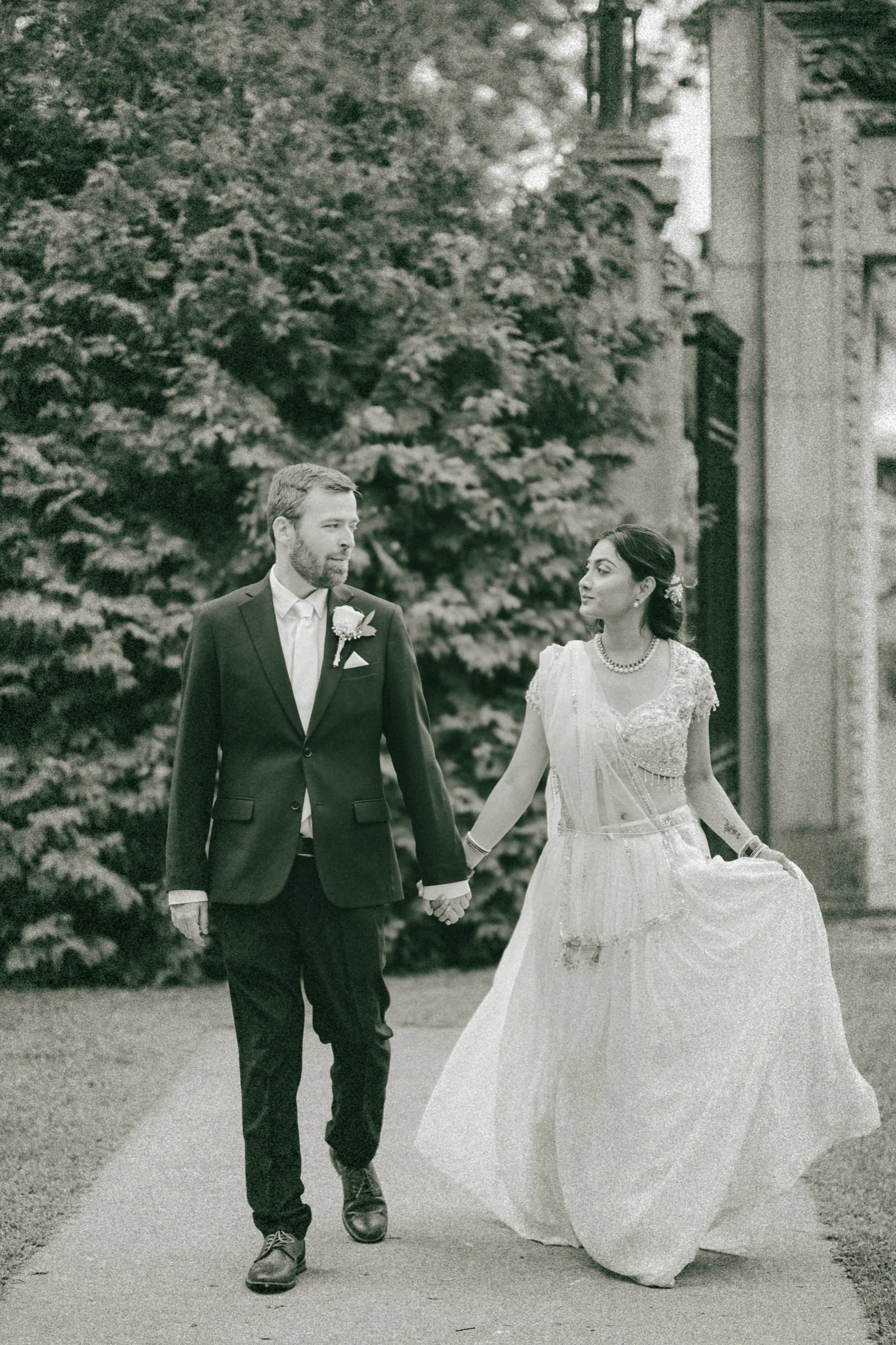 Black and white frame of Derek and Nidhi walking hand in hand down the path., by AD Photography