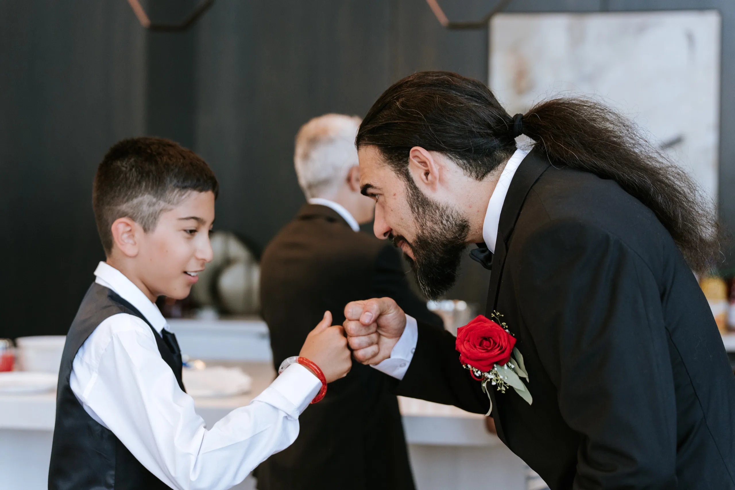 Moe fist bumps a young guest in a bow tie at the bar, by AD Photography