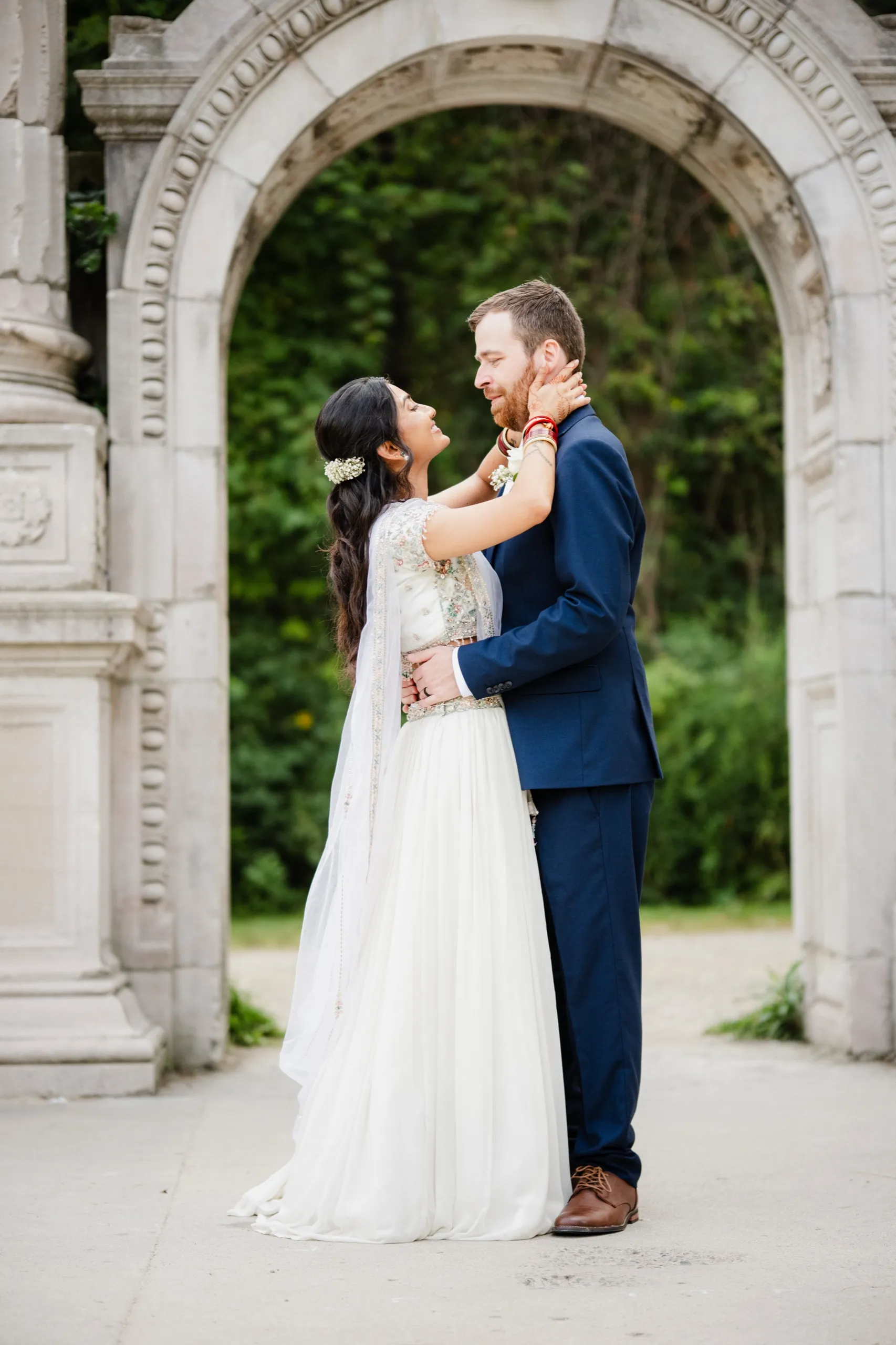 Nidhi cups Derek's face in a tender moment beneath the old stone arch., by AD Photography