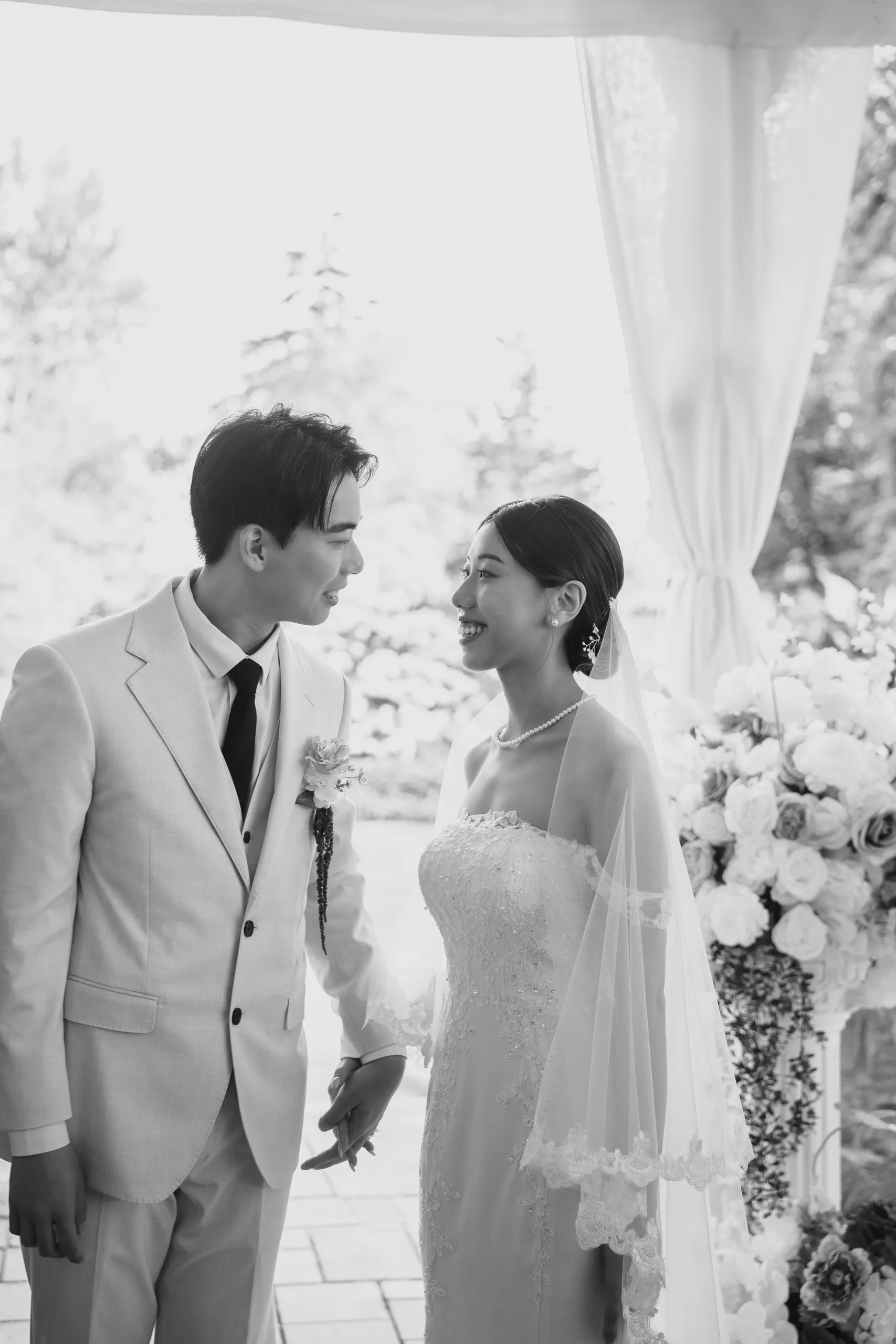 Black and white wedding portrait of Josie and Nelson holding hands beside the florals, by AD Photography