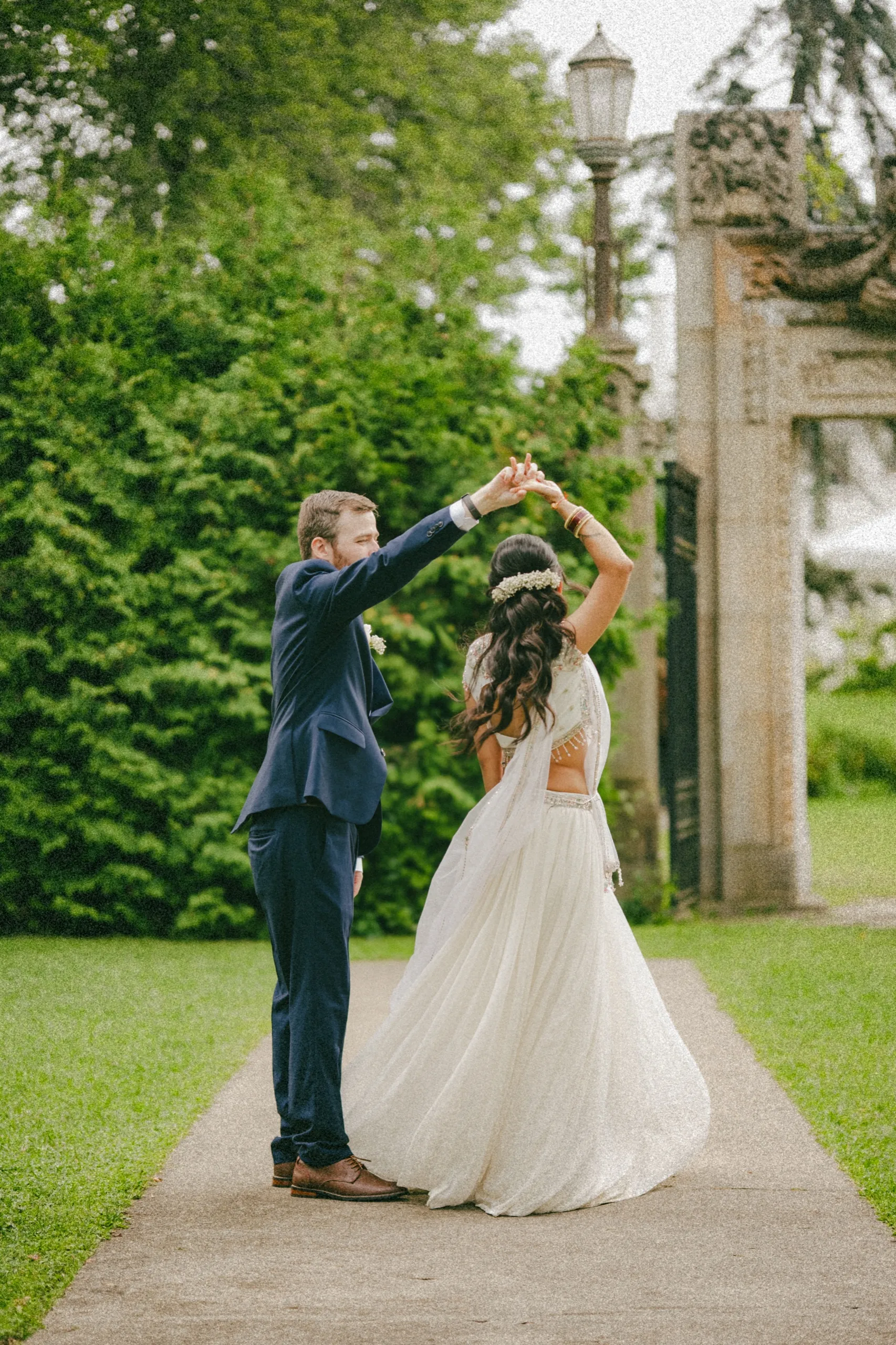 Derek twirls Nidhi under his arm on the garden path near the old lamppost., by AD Photography