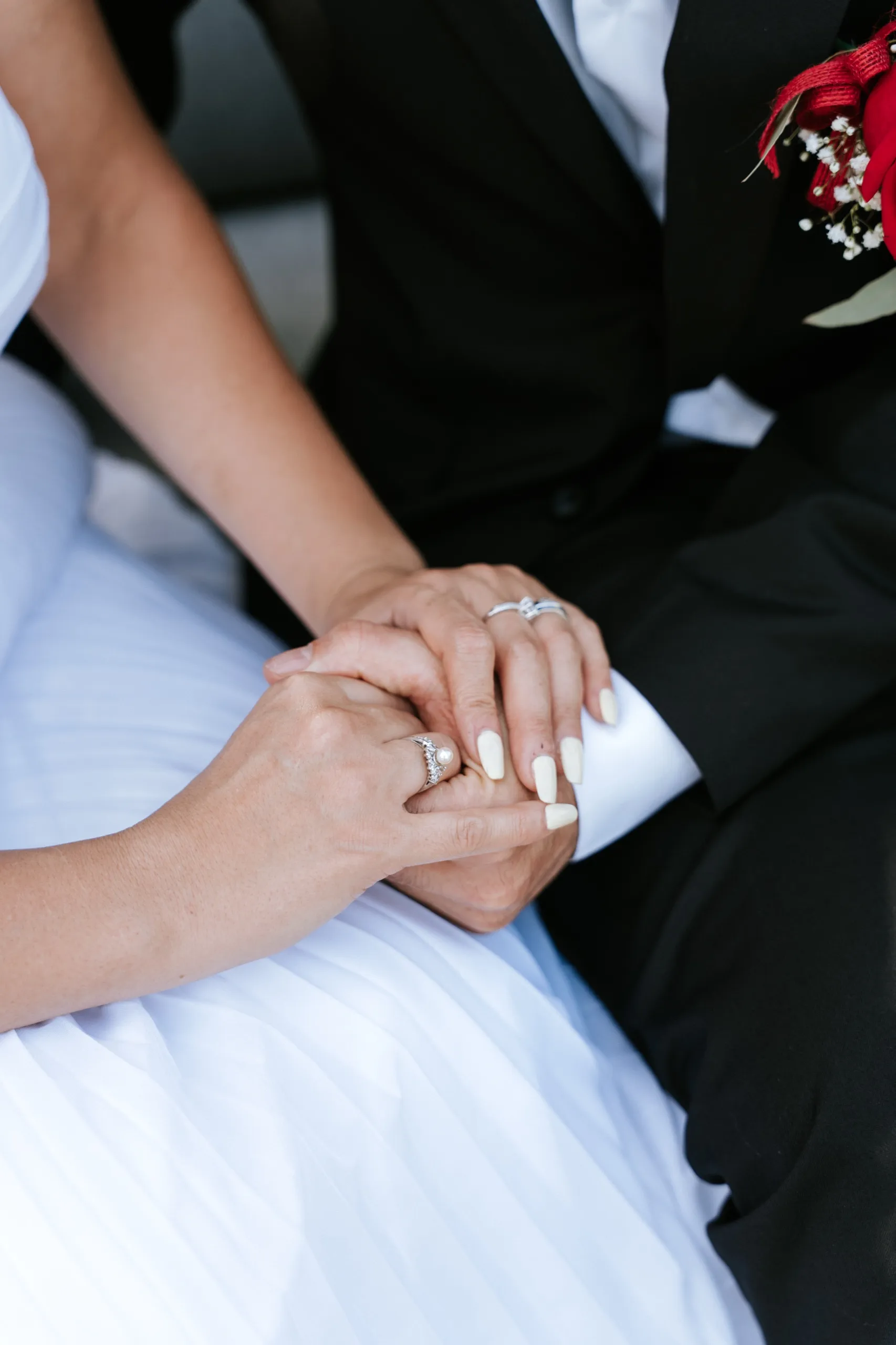 Zoha's hands resting over Moe's, rings and red boutonniere close in the frame, by AD Photography