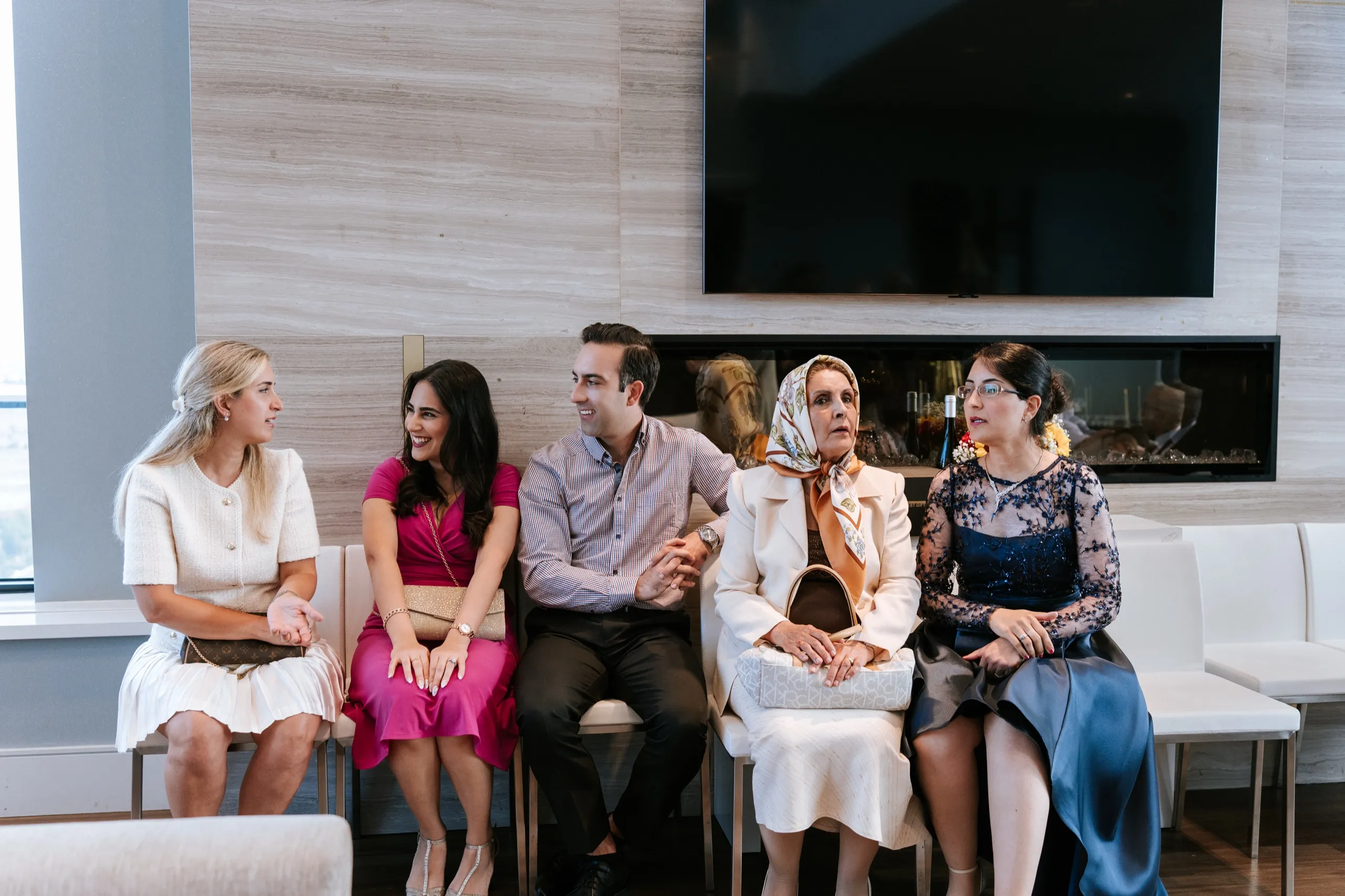 Five guests seated in a row along the fireplace bench, catching up mid celebration, by AD Photography