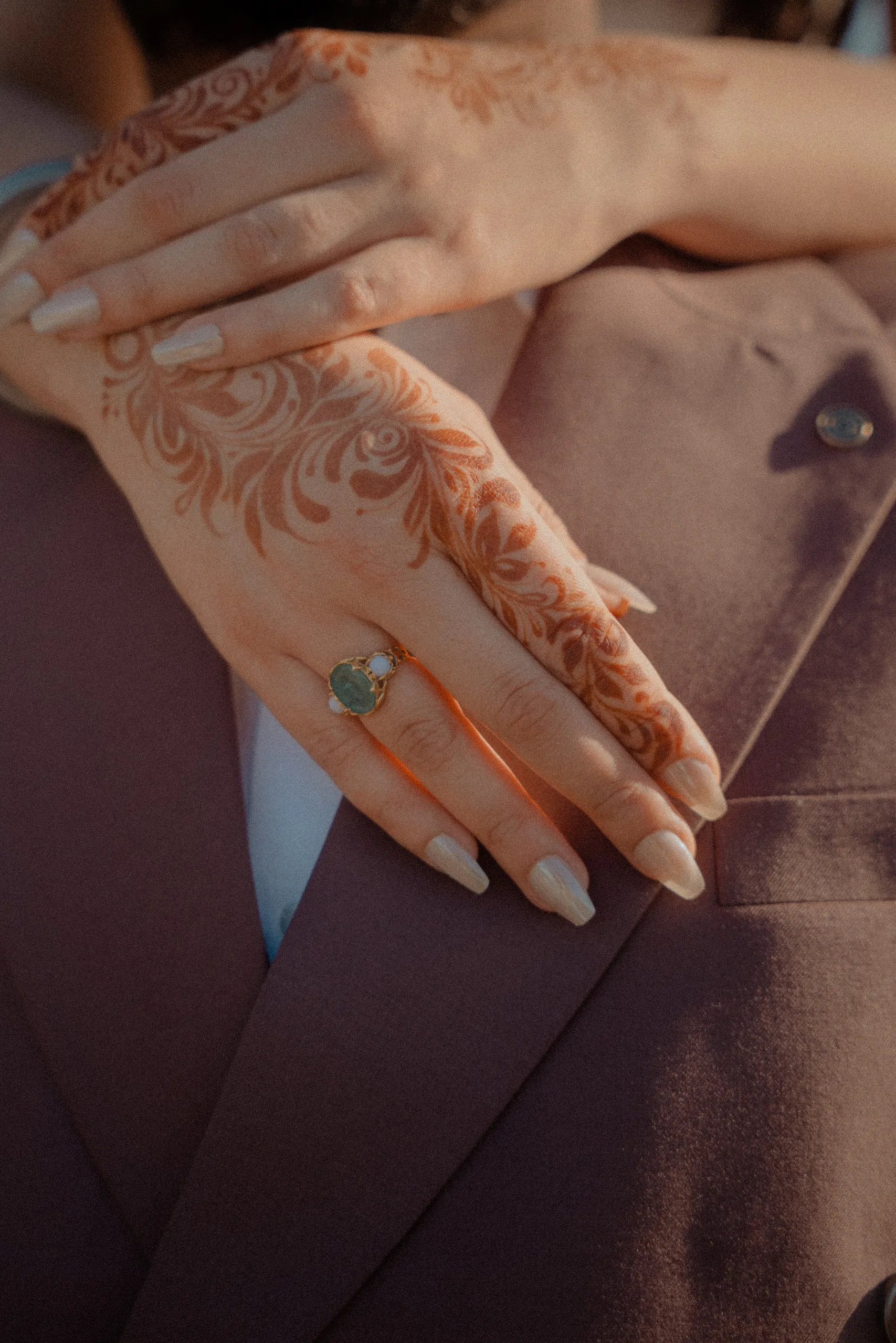 Henna covered hands and a jade ring resting against the groom's mauve lapel, by AD Photography