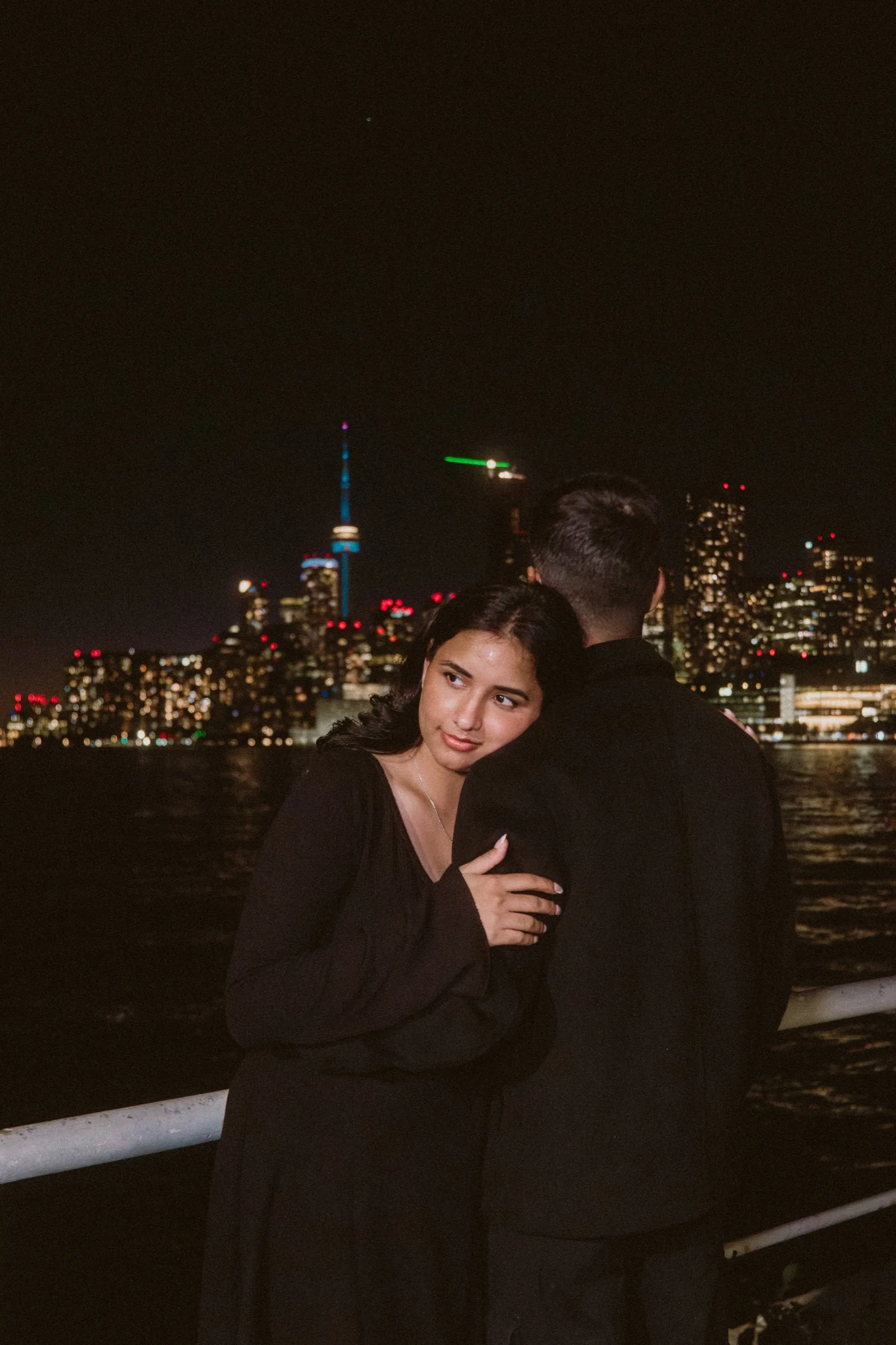 Swati rests her cheek on Saksham's shoulder, skyline lights scattered across the dark, by AD Photography
