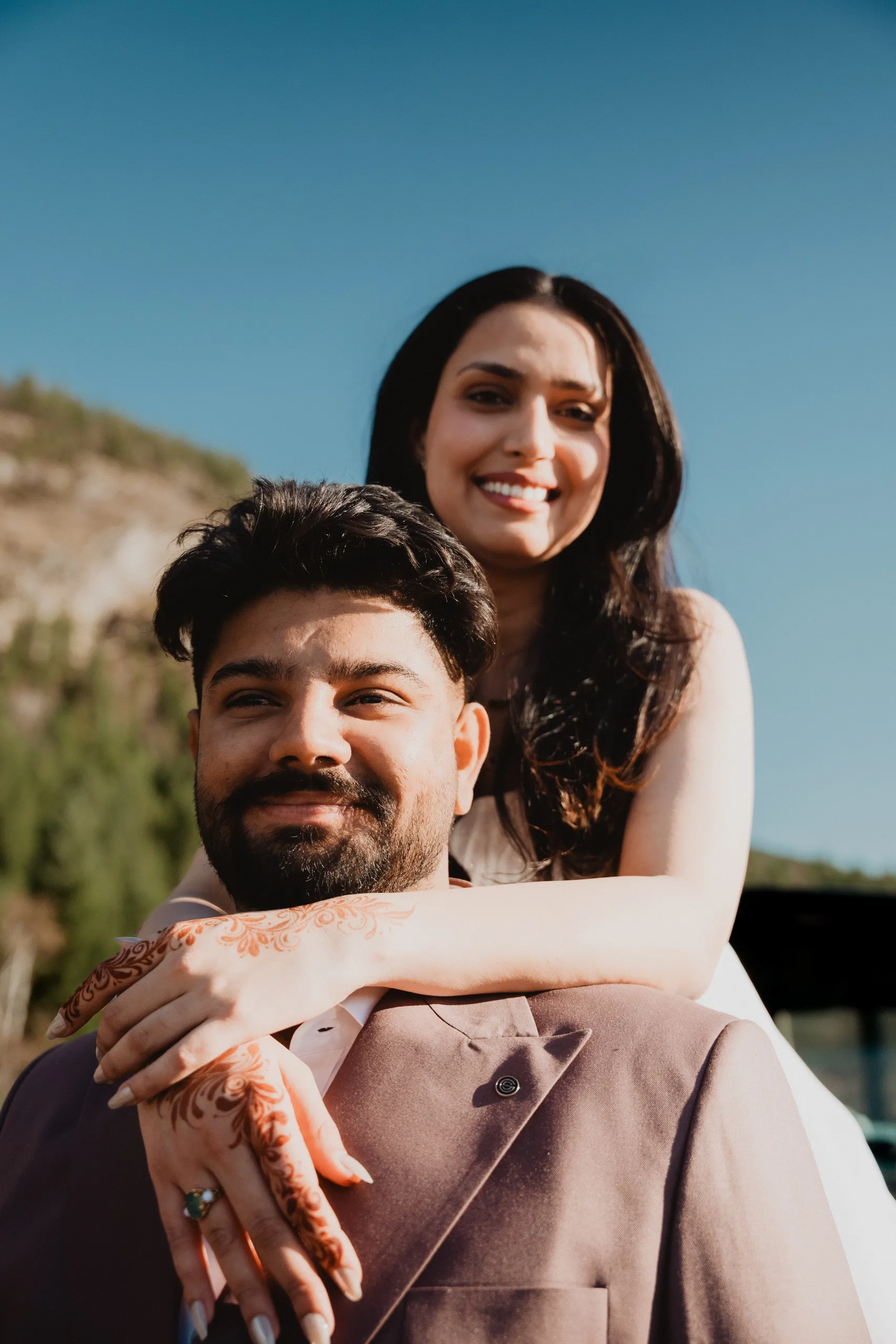 Mehak leaning over Kamal's shoulder from the truck bed, henna hands crossed on his chest, by AD Photography