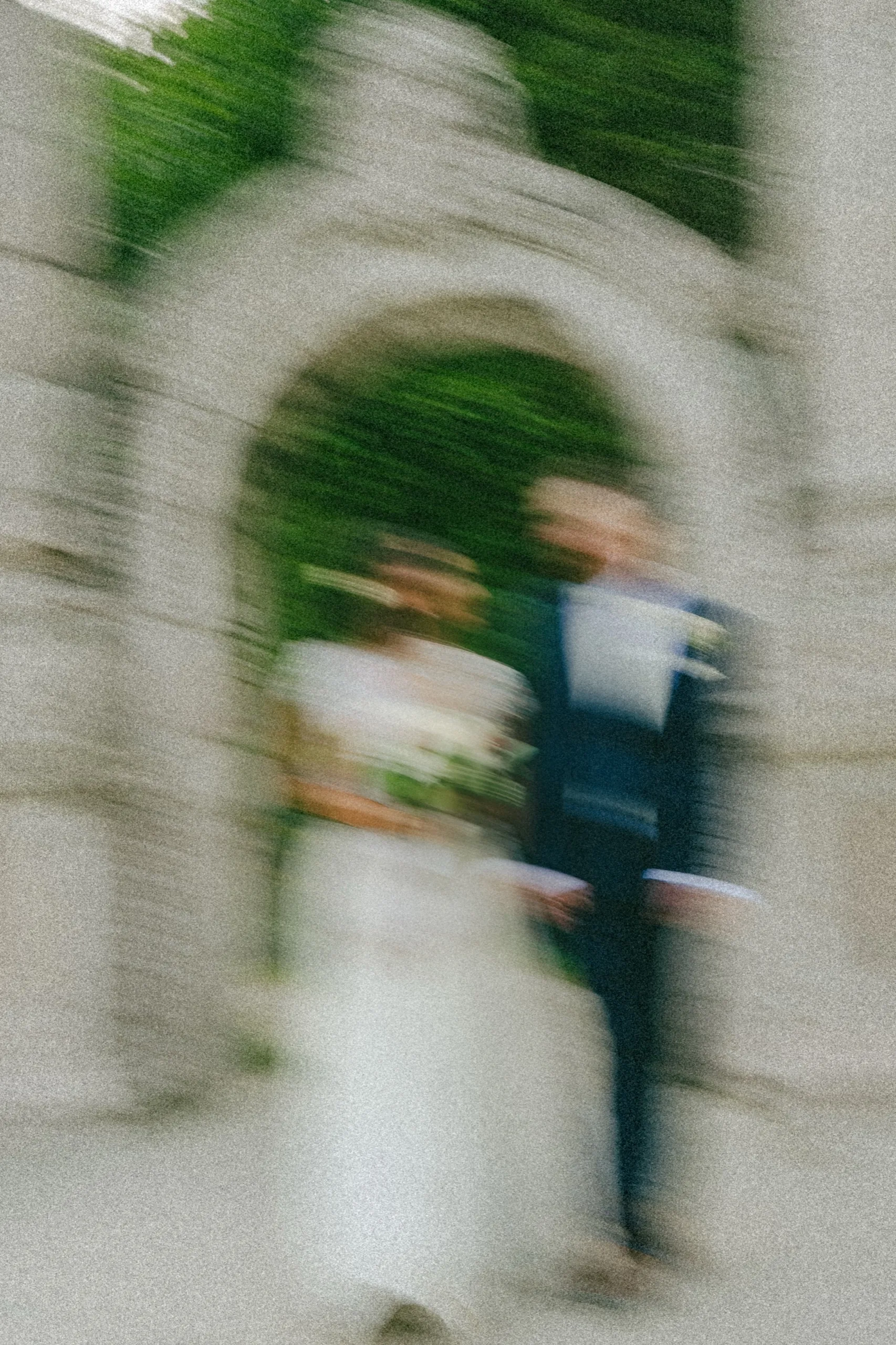 Grainy film style frame of Nidhi and Derek walking arm in arm through the stone arch., by AD Photography
