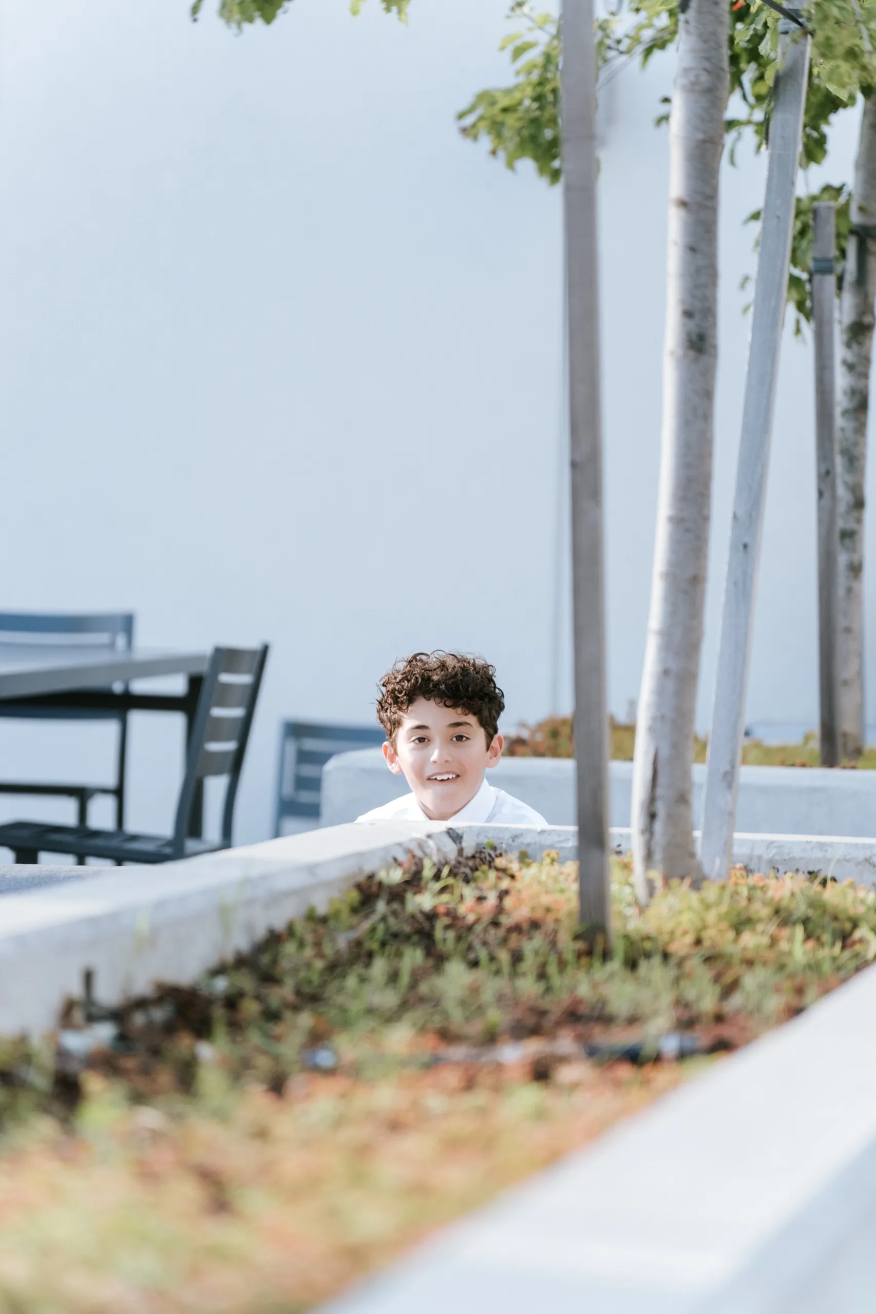 A boy peeks over the terrace planter, framed through the ornamental grasses, by AD Photography