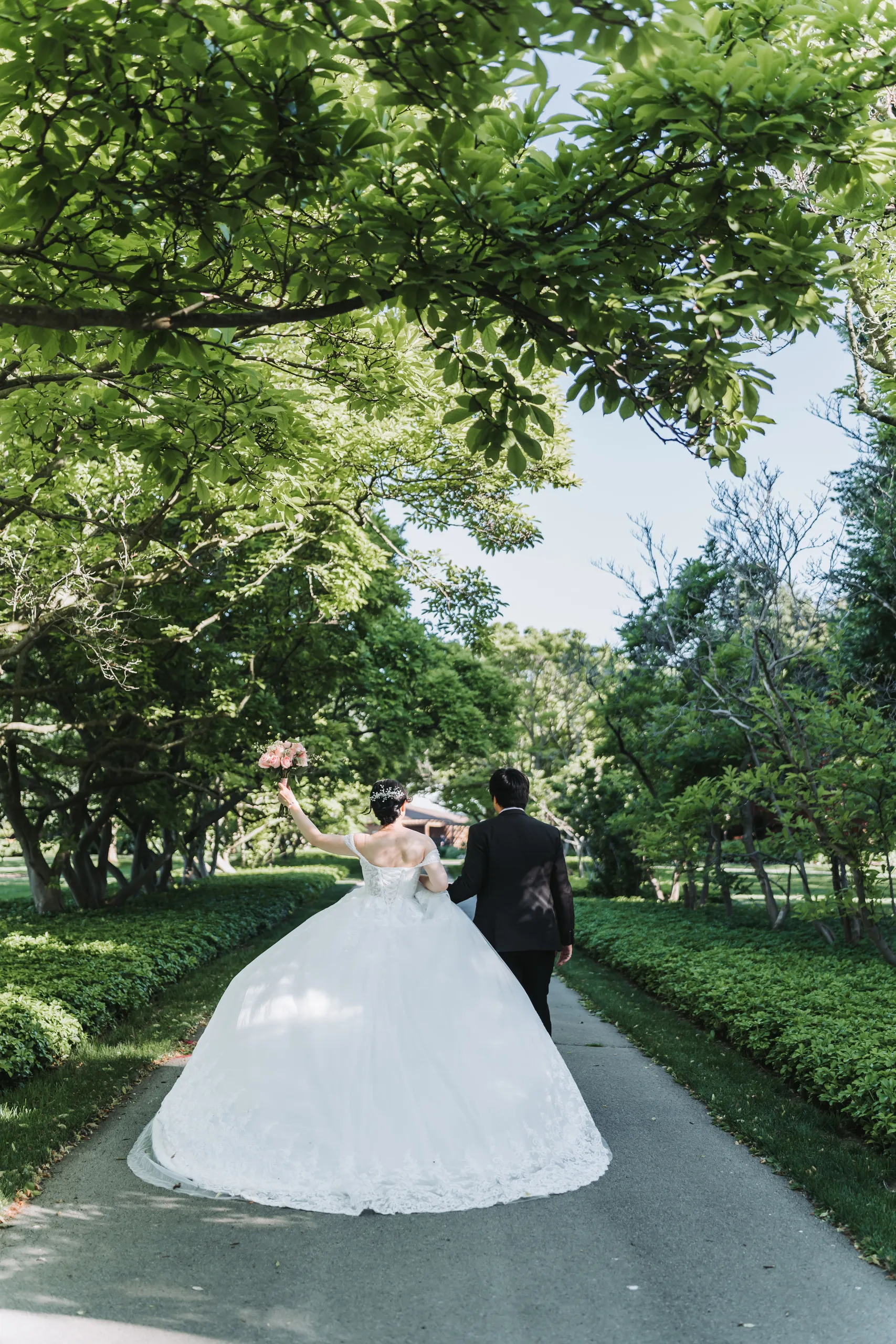 Karen raising her bouquet as Micheal glances back on a Botanical Gardens path in Niagara Falls, by AD Photography