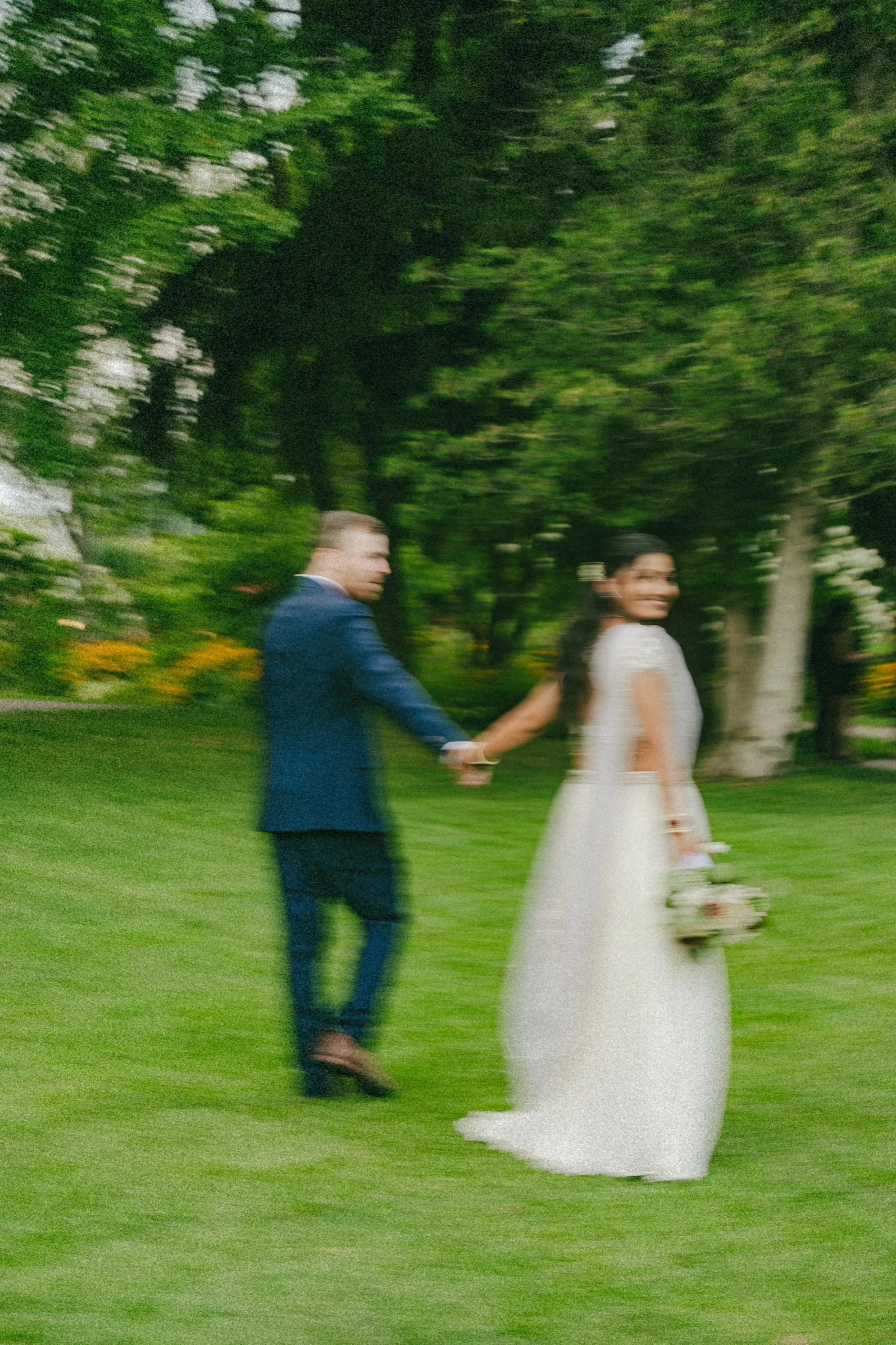 Grainy motion blur of Nidhi glancing back at Derek as they cross the lawn together., by AD Photography