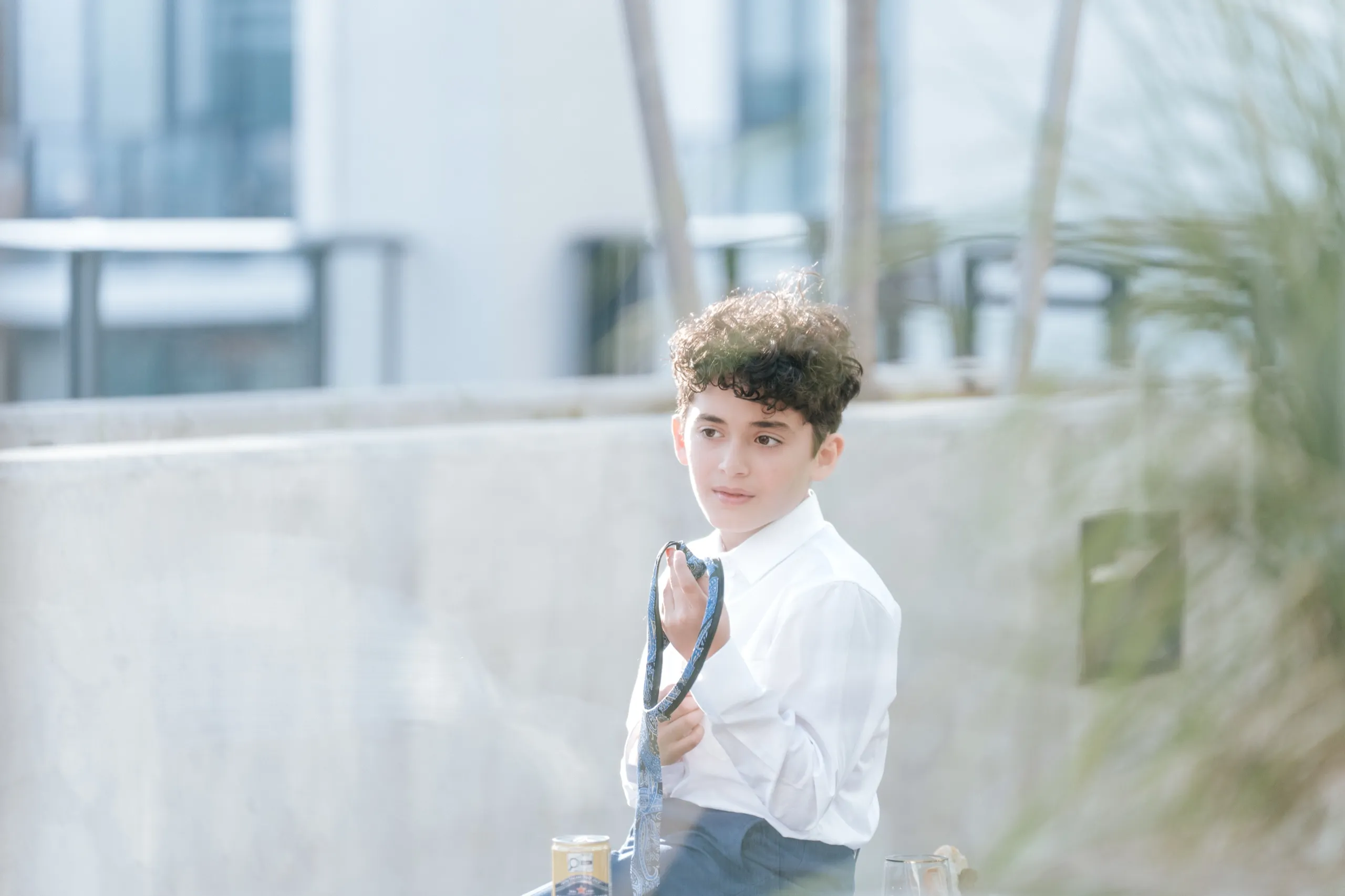 A boy on the terrace fixing his tie in hazy afternoon backlight, by AD Photography