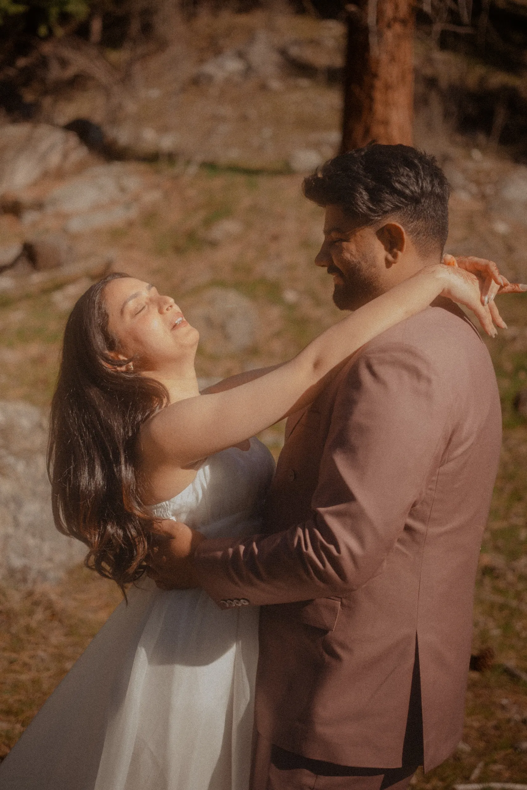 The bride leaning back laughing with her arms around Kamal's neck on the hillside, by AD Photography