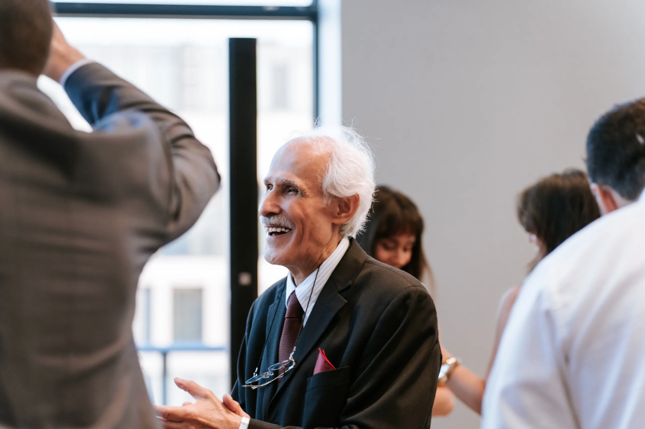 A family elder laughing mid conversation across the crowded room, by AD Photography