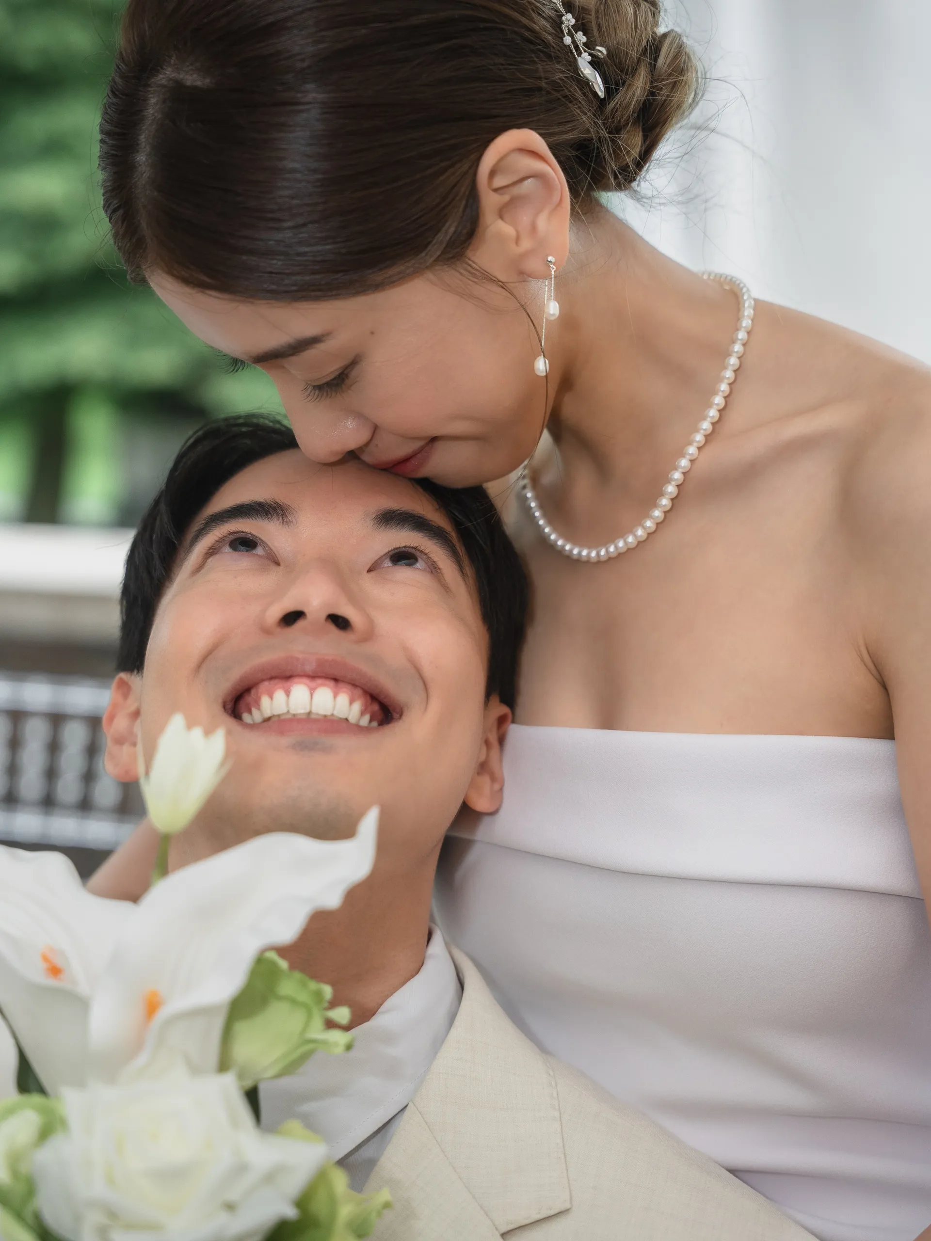 Josie kissing Nelson's forehead as he looks up laughing, white calla lilies in front, by AD Photography