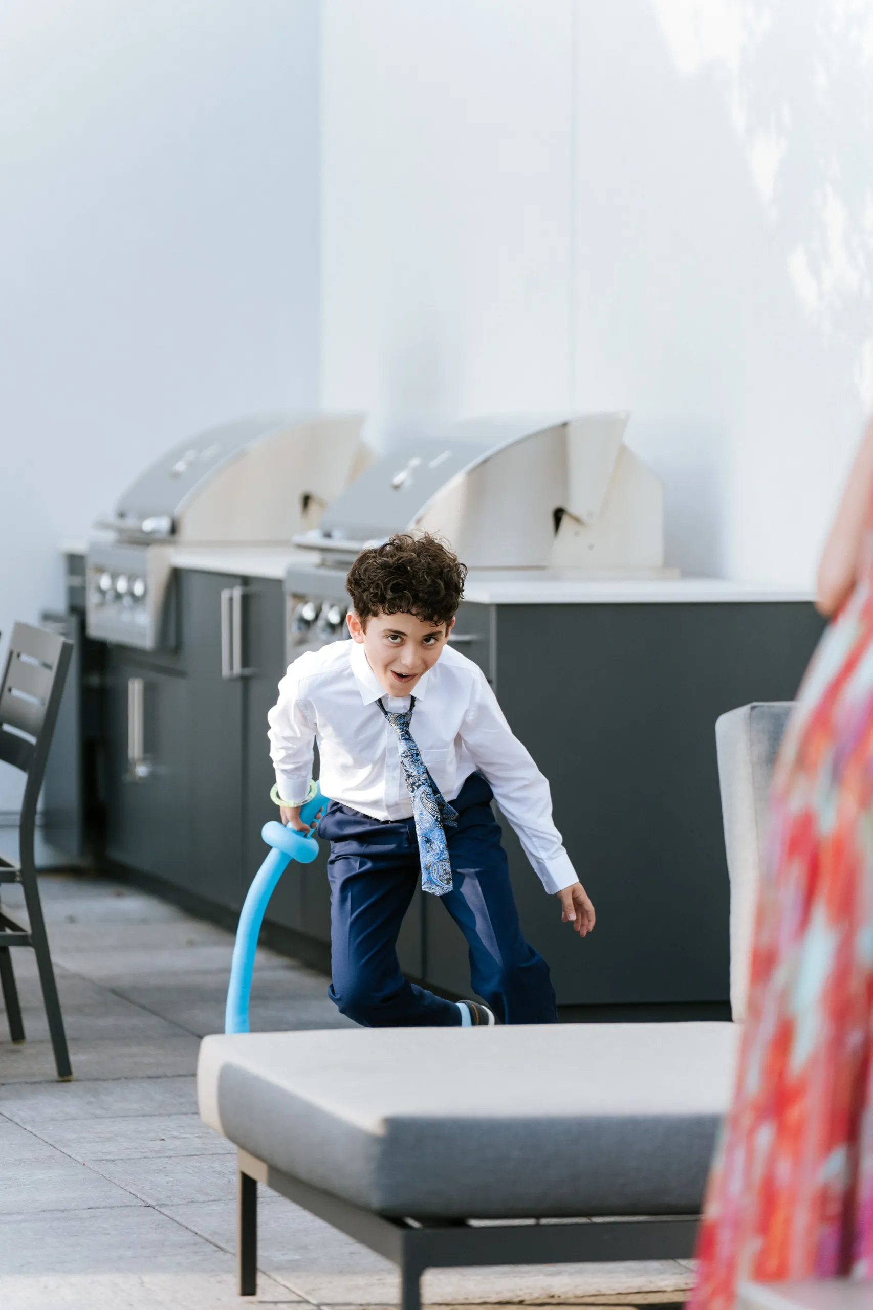A boy runs past the terrace grills with his blue balloon sword, by AD Photography