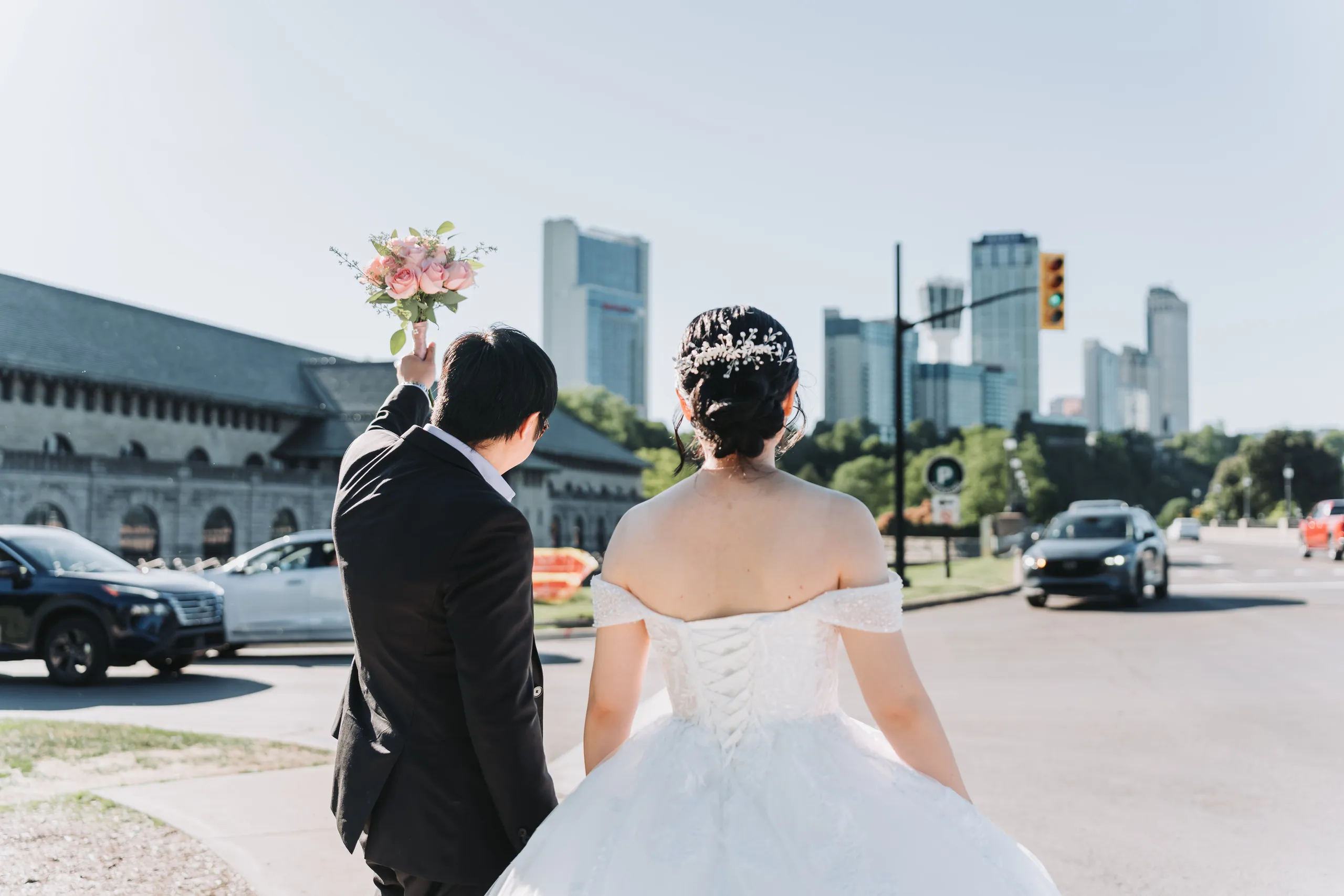 Karen raising her bouquet overhead on the Niagara Parkway with the Falls skyline behind, by AD Photography