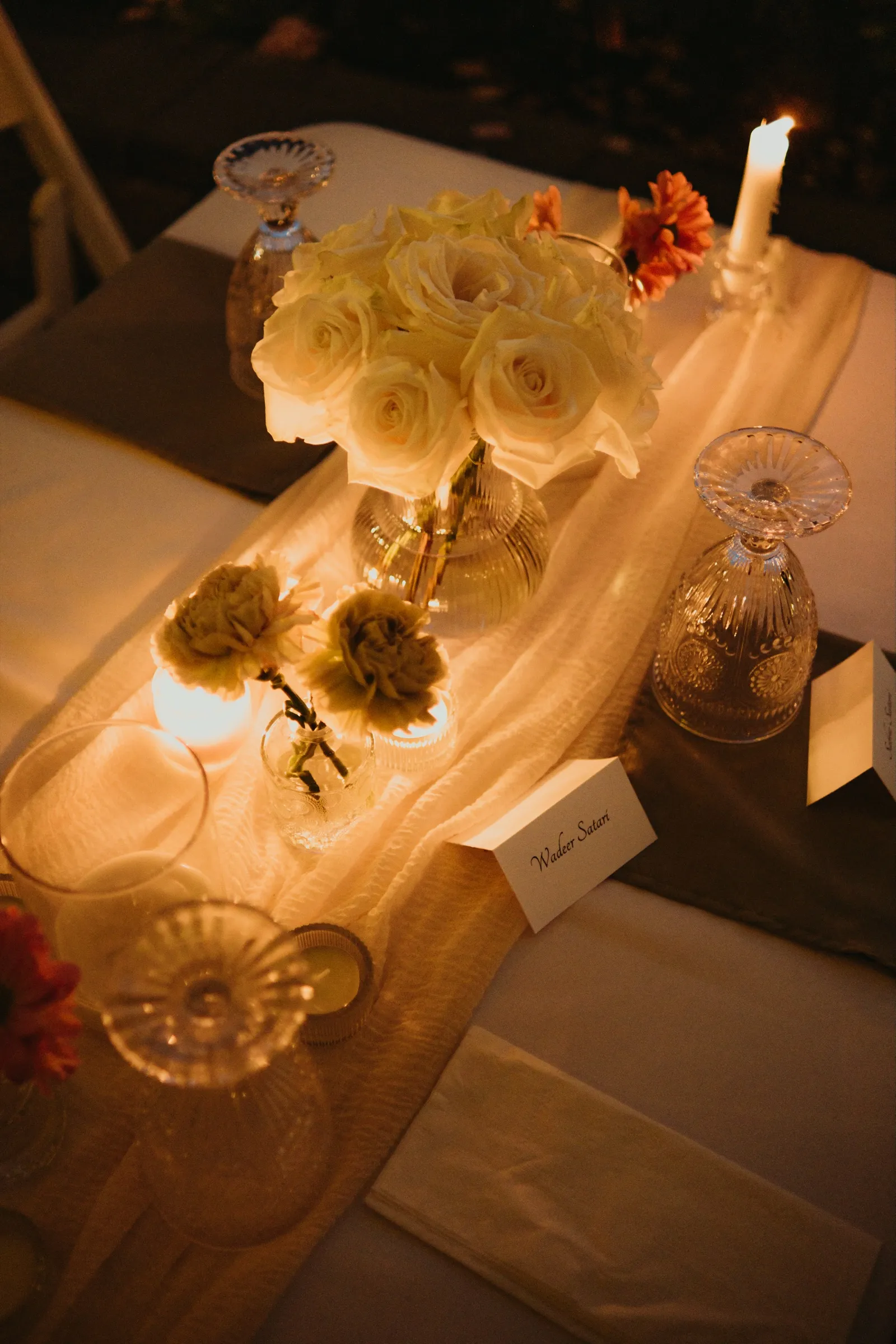 Crystal goblets, garden roses and a handwritten place card in soft candle glow, by AD Photography