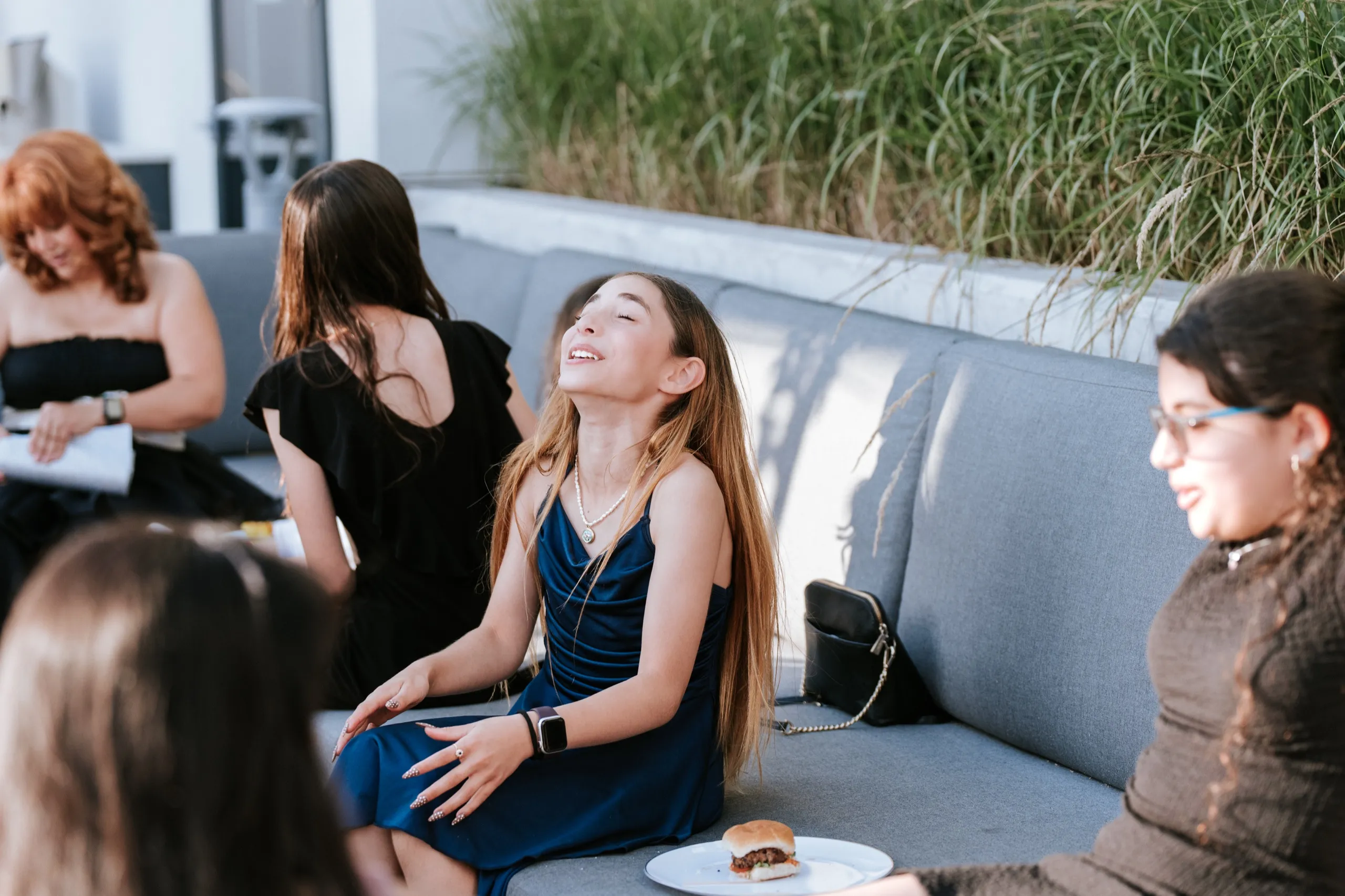A girl laughs with her head thrown back on the terrace couch, her plate at her side, by AD Photography