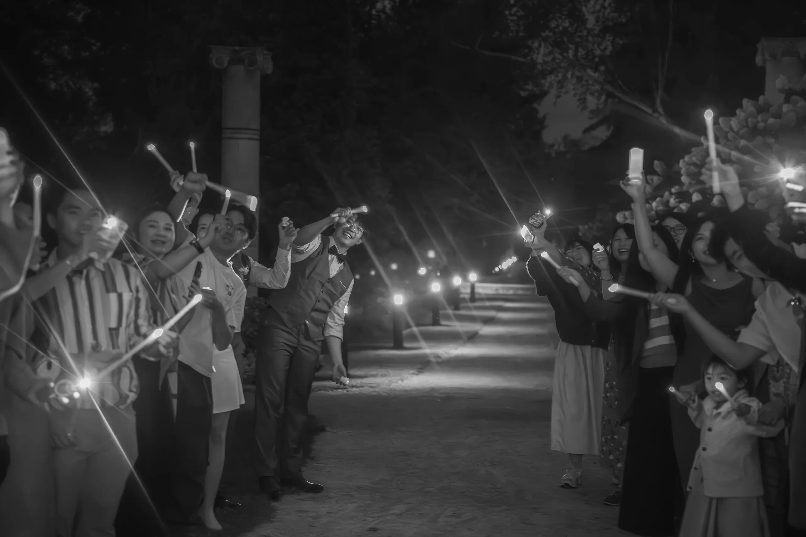 Black and white wedding send off, guests raising candles in a tunnel along the path, by AD Photography