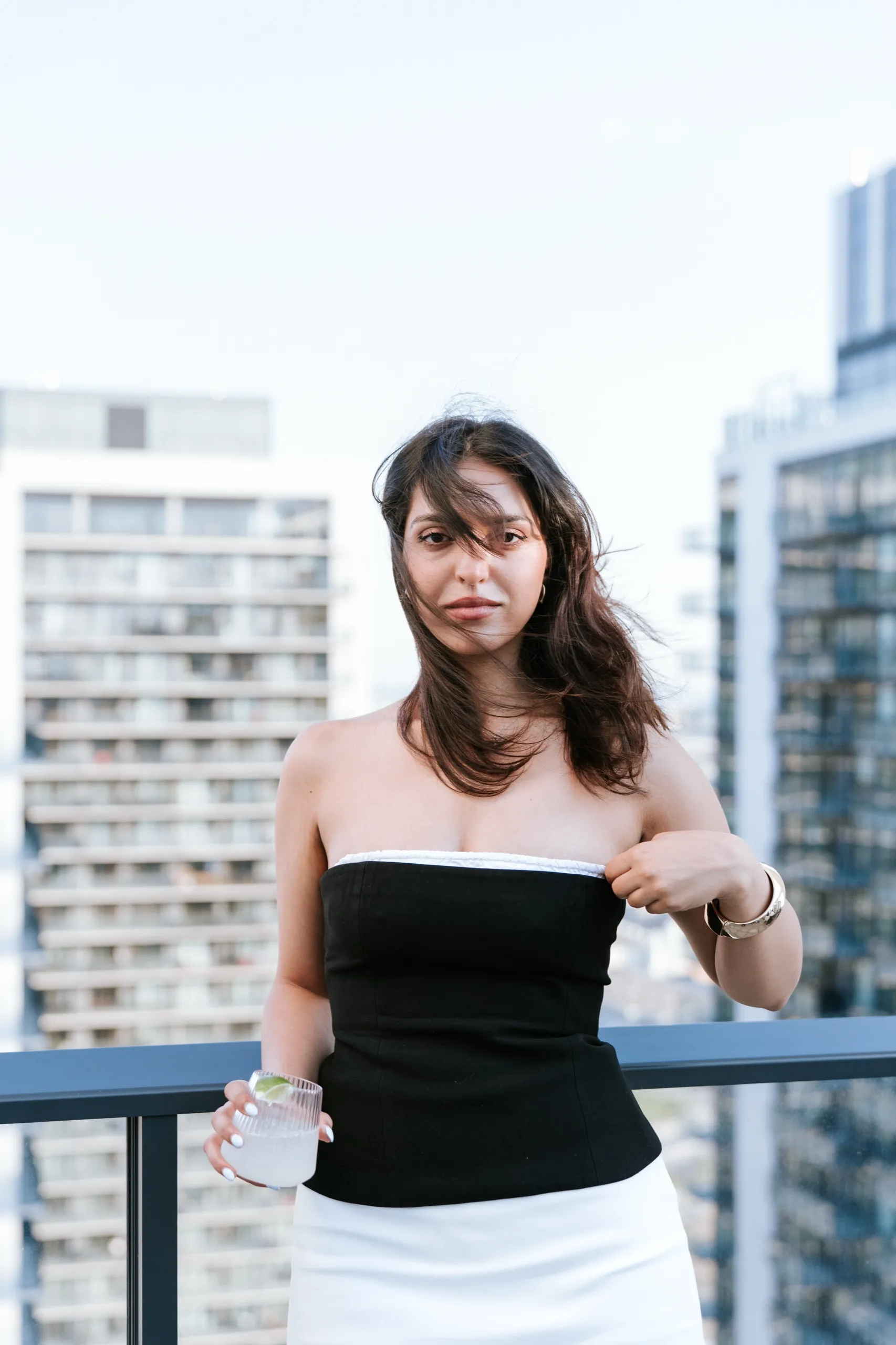 A guest with a drink at the terrace railing, Maple condo towers stacked behind her, by AD Photography
