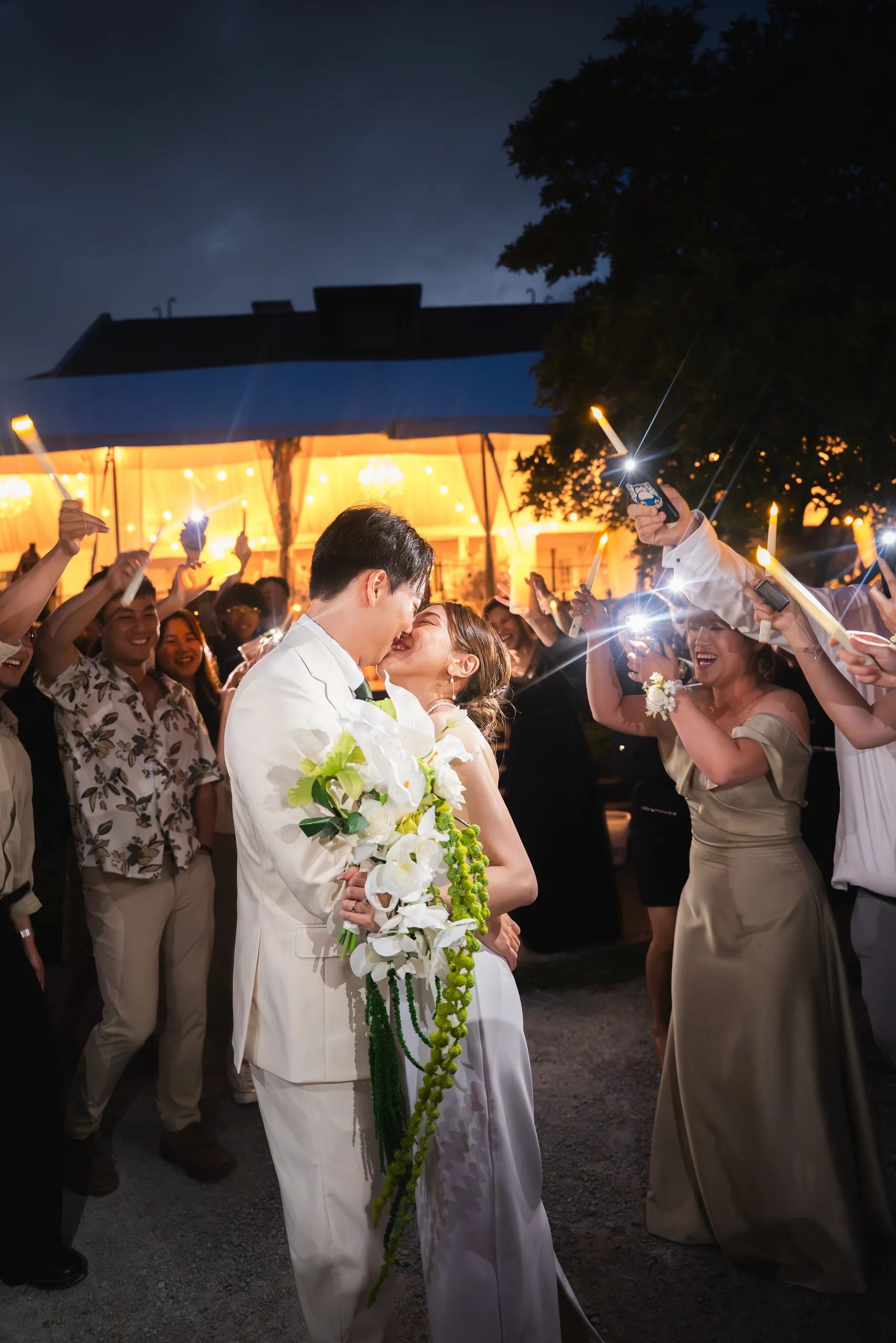 Night kiss beneath raised candles as guests cheer outside the glowing Guild Park tent, by AD Photography