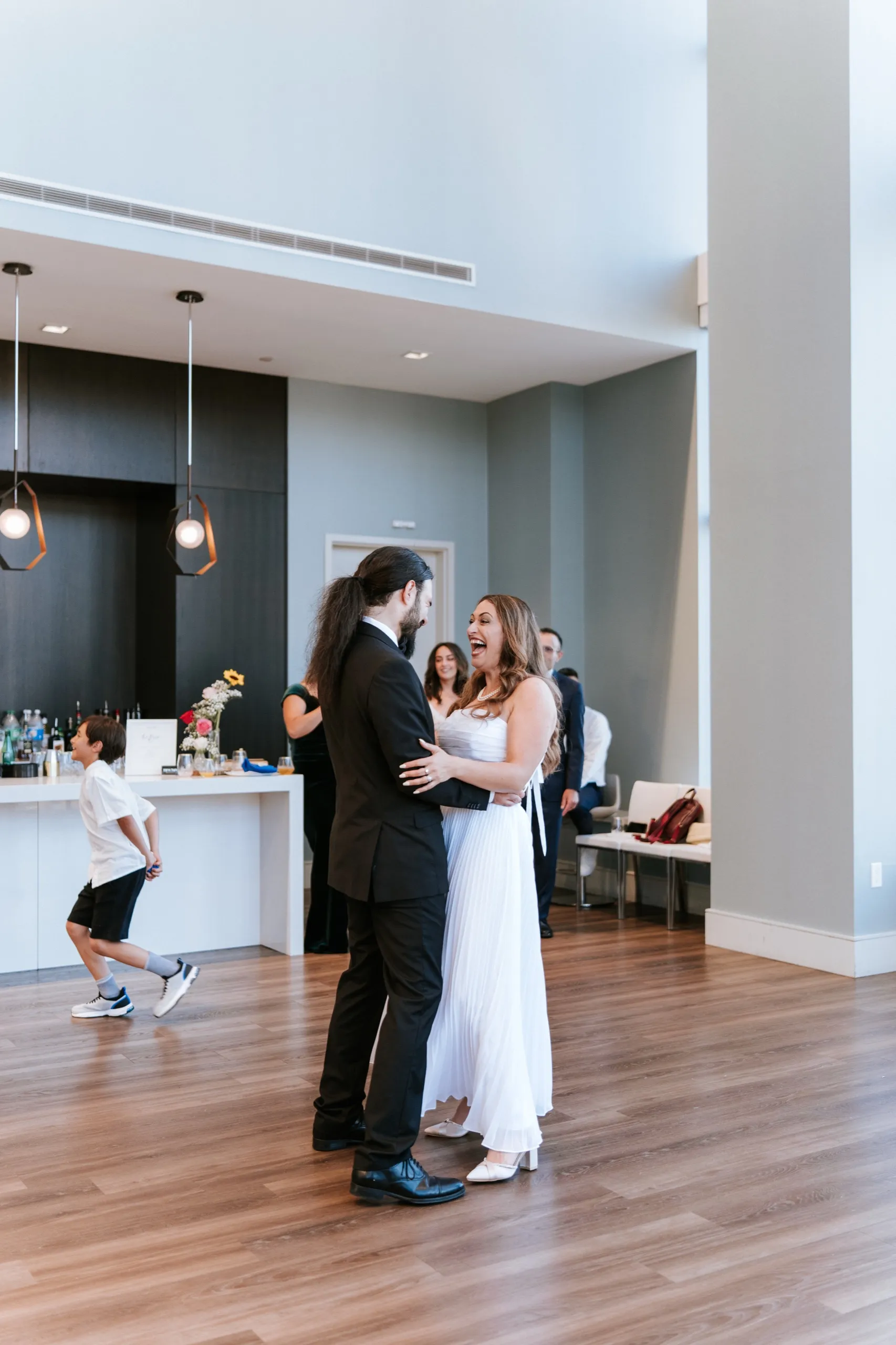 Zoha and Moe dance on the open floor while a boy runs past the bar, by AD Photography