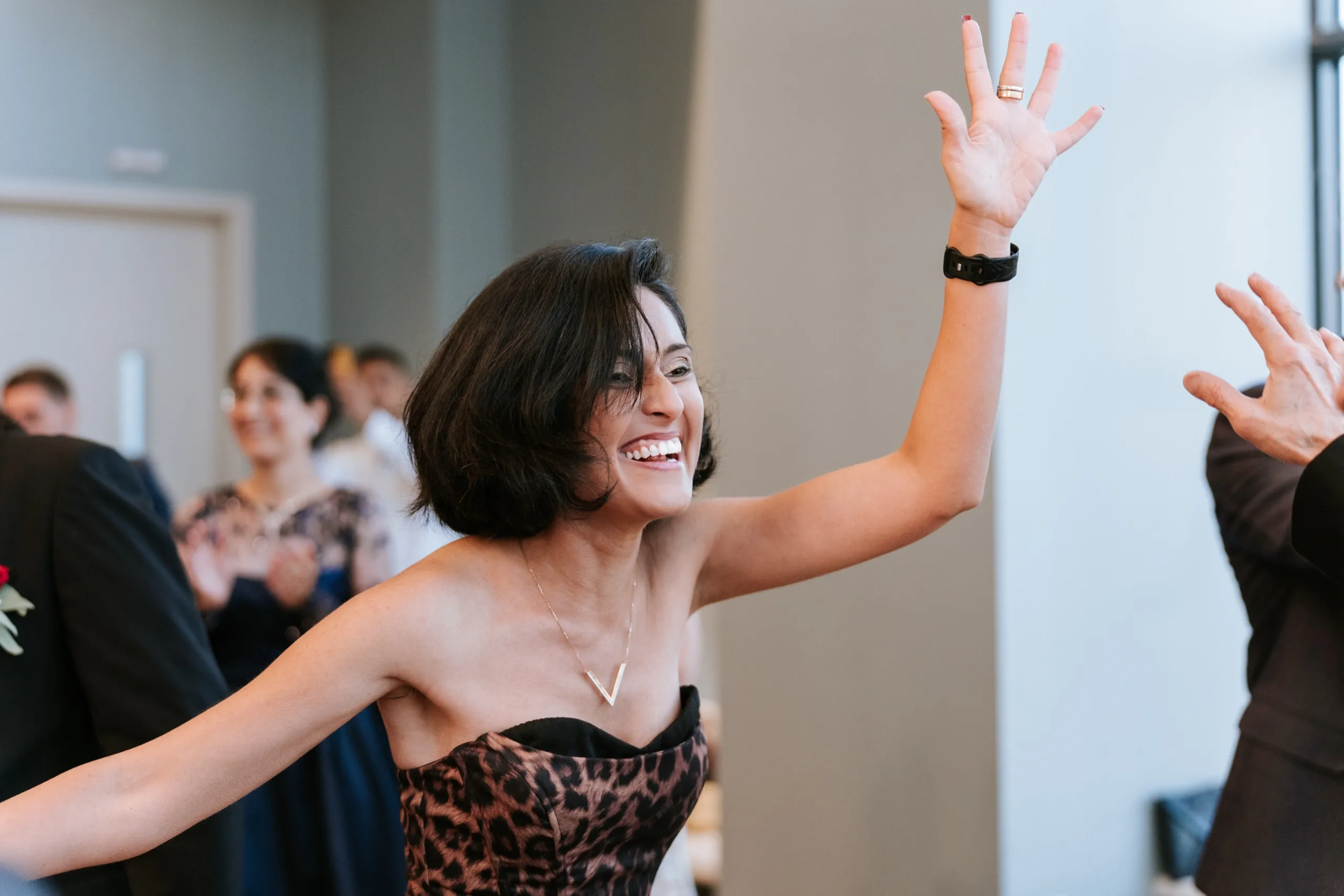 A guest in a leopard print dress throws an arm up, laughing on the dance floor, by AD Photography