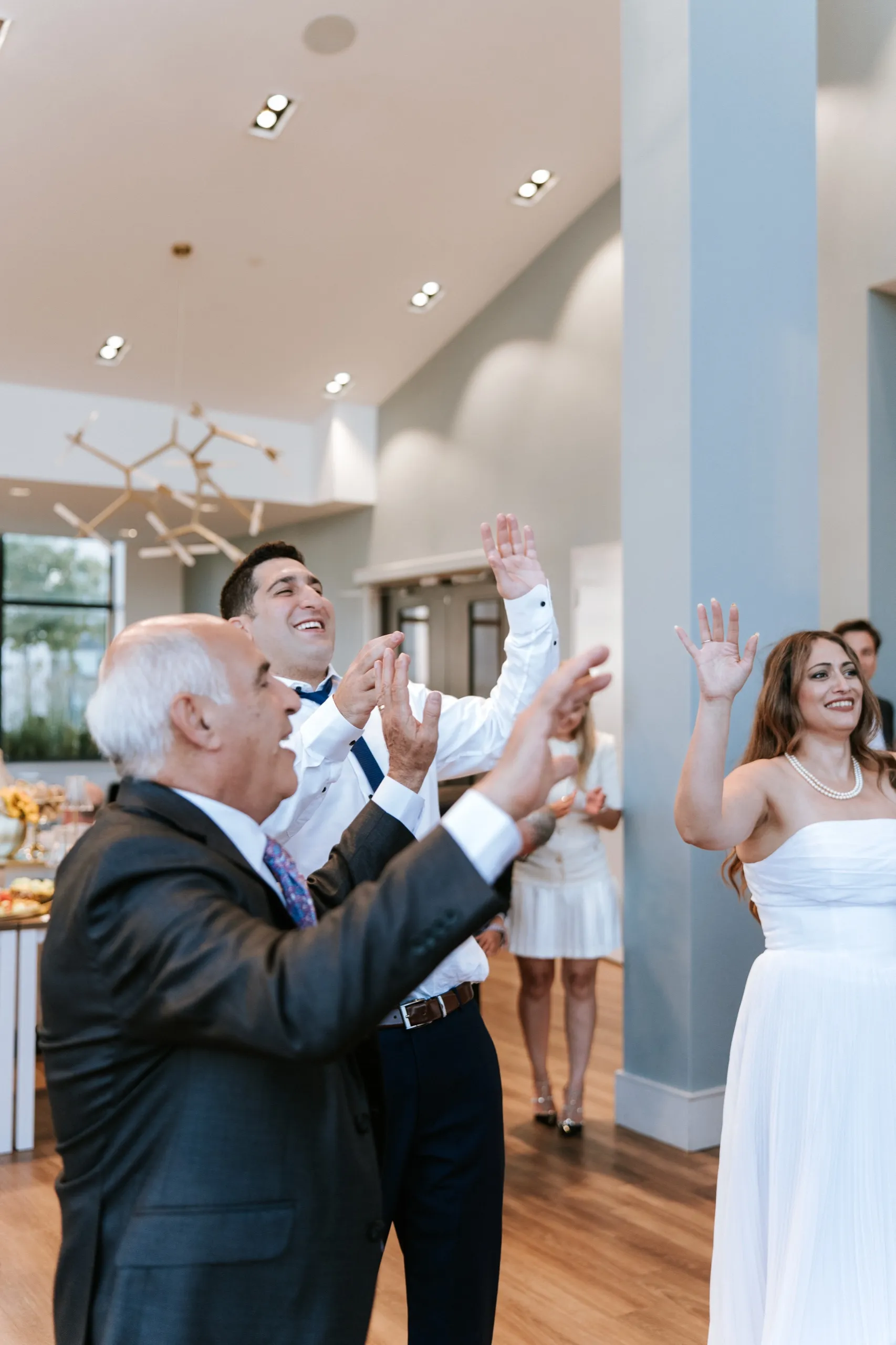 Two guests clap with their hands high as Zoha keeps dancing beside them, by AD Photography