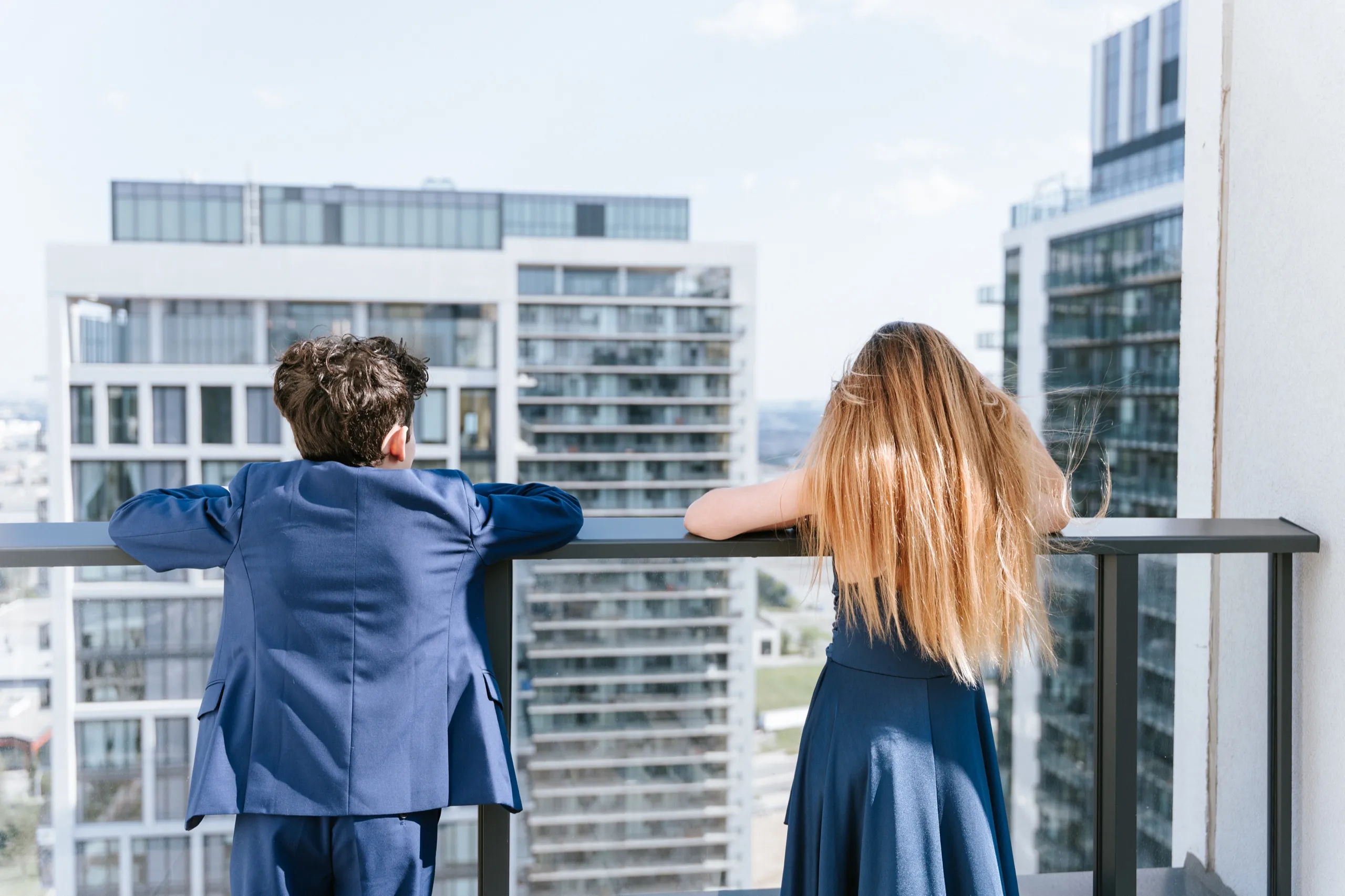 Two kids lean on the terrace railing looking out at the condo towers in Maple, by AD Photography