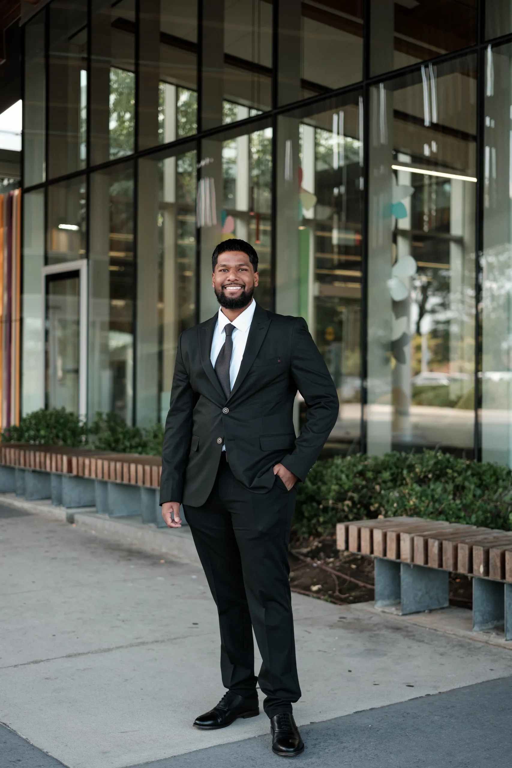 A full length business portrait on the sidewalk outside Albion Public Library, benches and planters in the background, by AD Photography